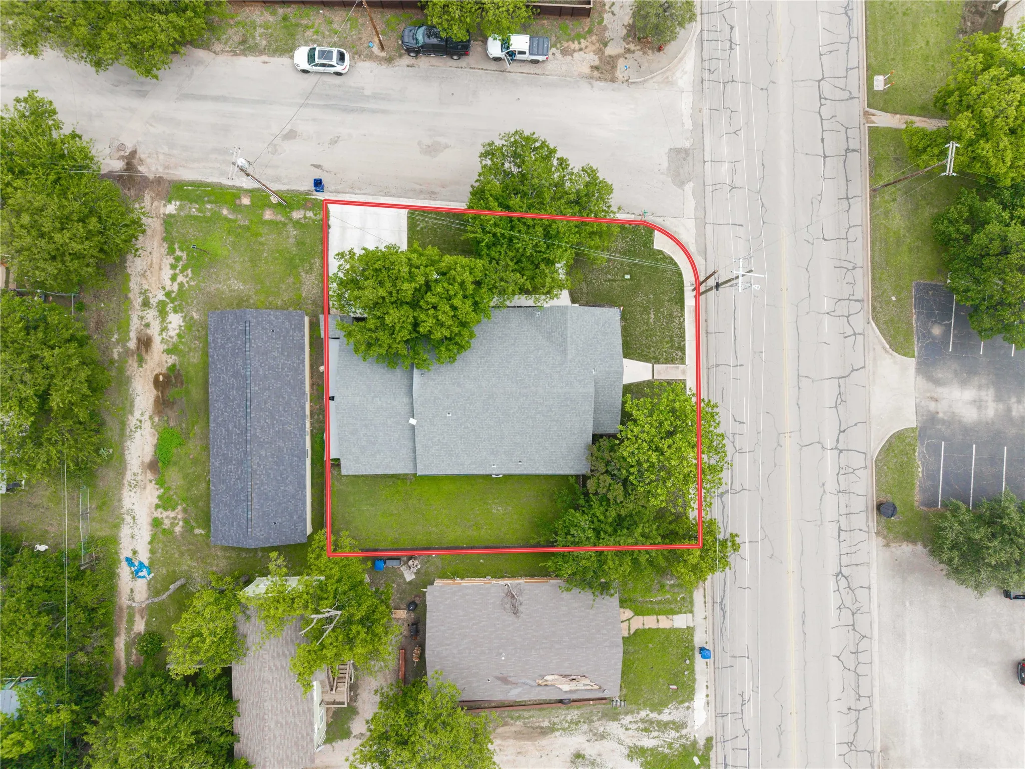 Aerial view of a property featuring a corner lot with an asphalt shingle roof, established trees, and a grassy yard