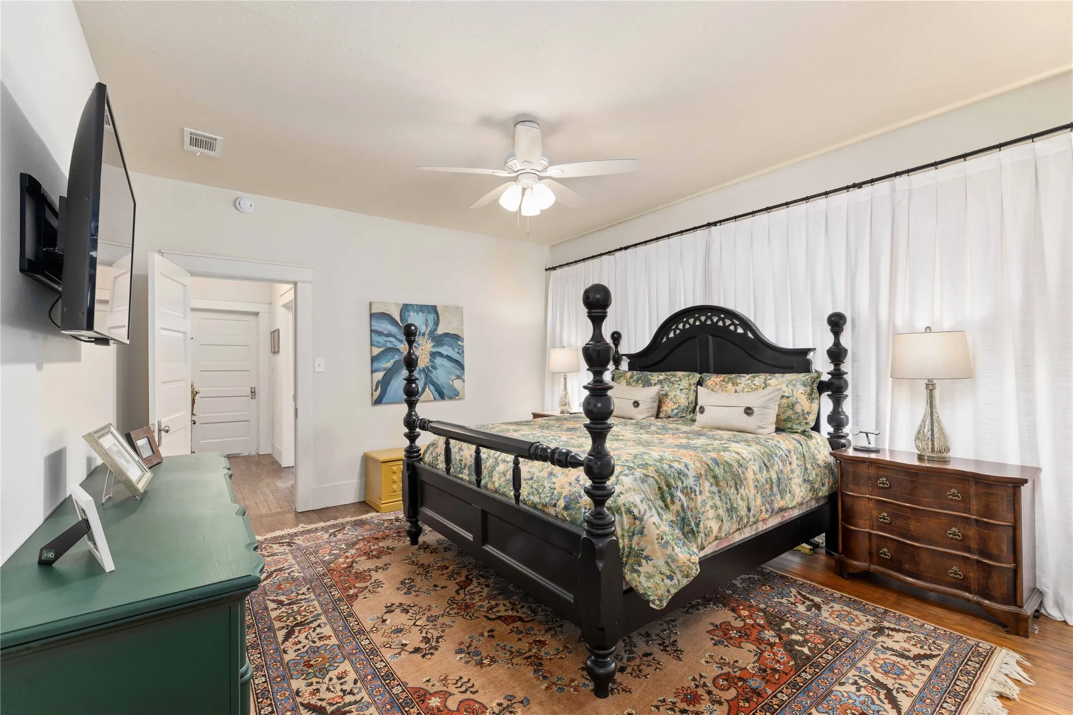 Bedroom featuring wood-finish flooring, a ceiling fan, and white window treatments