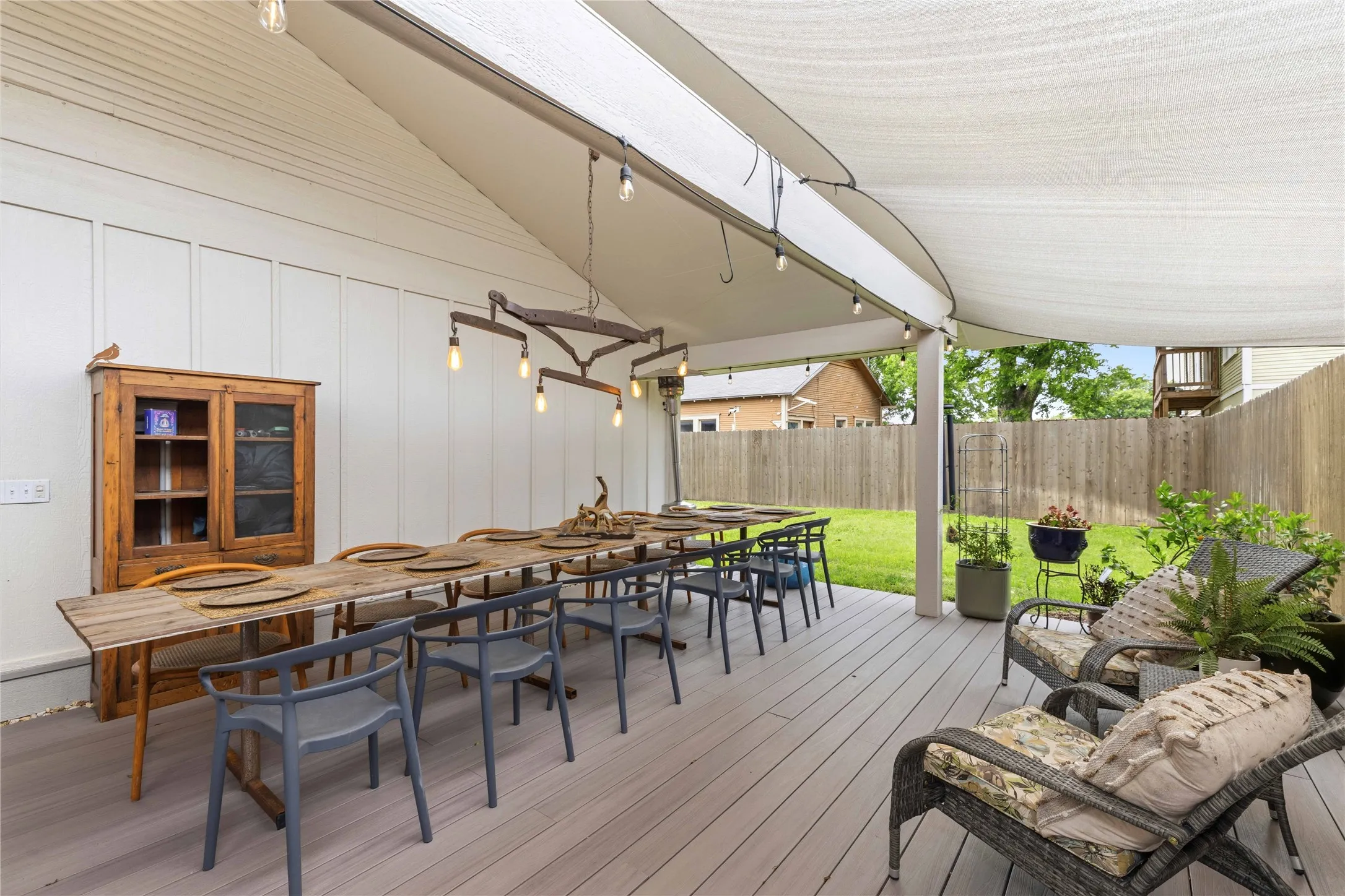Spacious outdoor deck featuring light-colored composite flooring, a white panel accent wall, and a large shade canopy