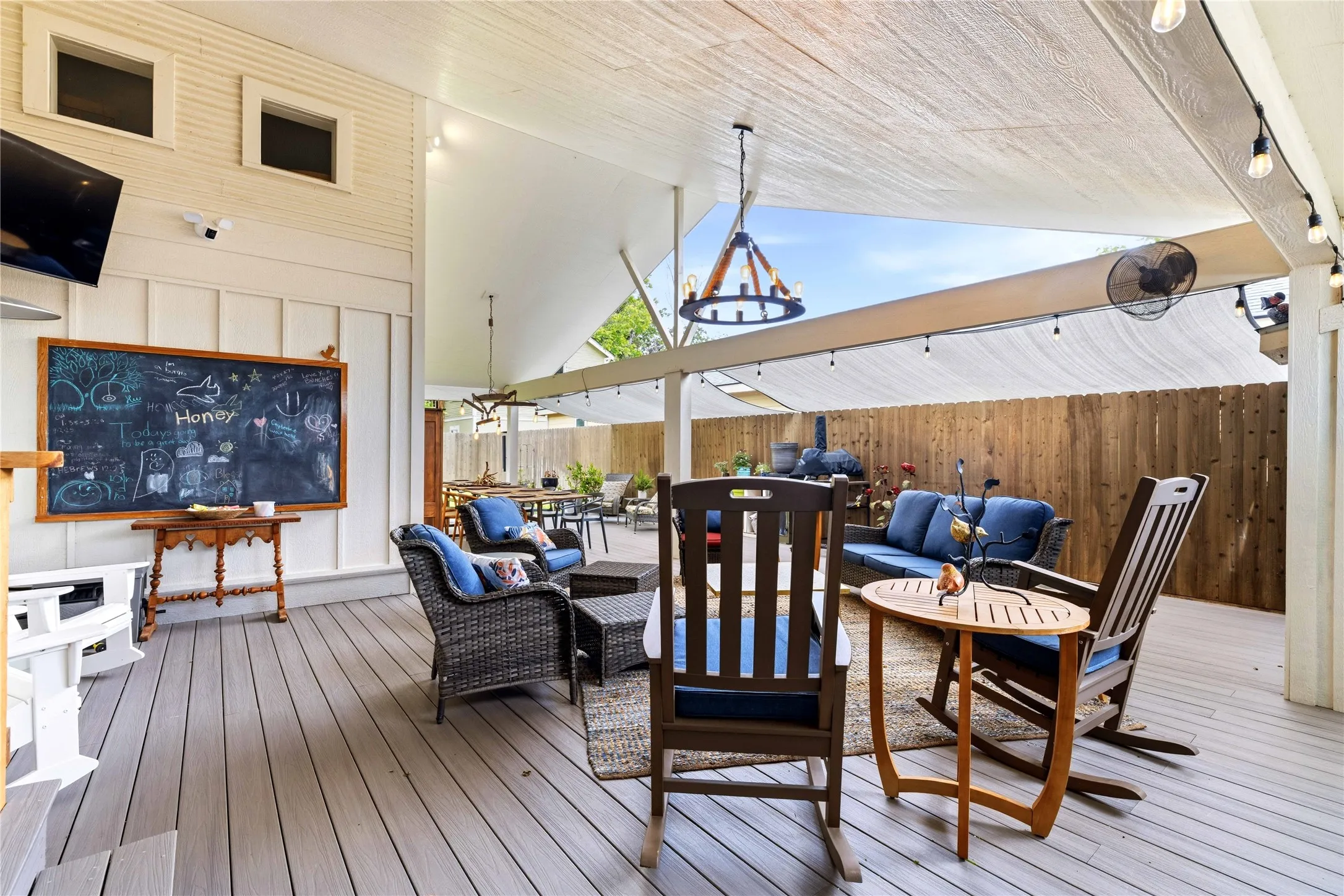 Expansive covered patio featuring wood-finish decking, a vaulted ceiling, string lighting, and a privacy fence