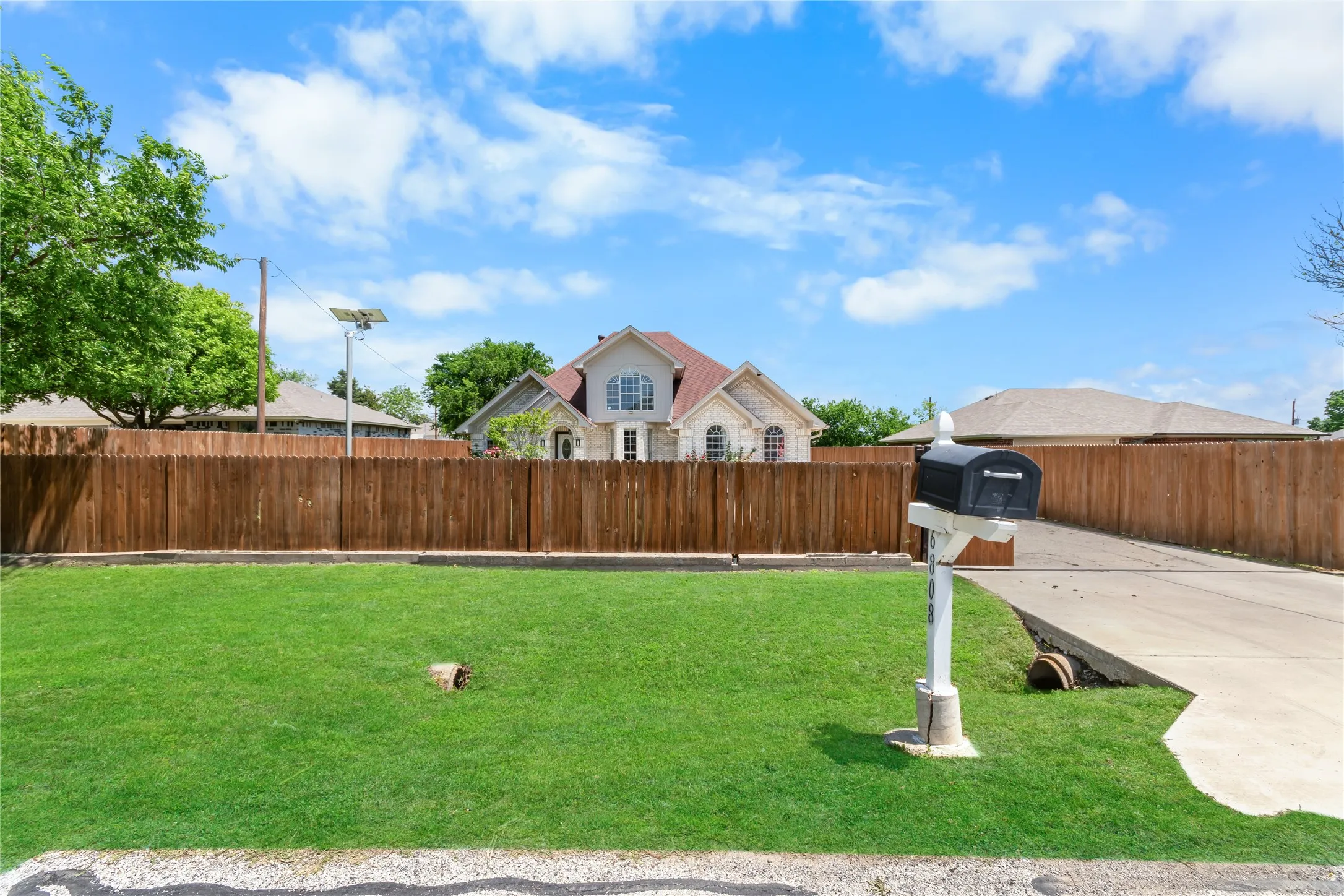 Street View. Fully gated property with a concrete driveway and a mailbox on a white post