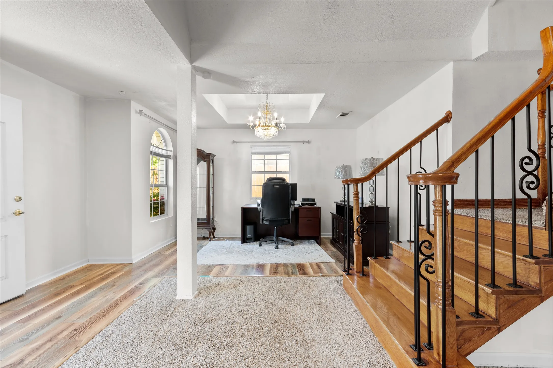 Foyer featuring a wood-finish staircase with wrought iron balusters, light-toned carpeting, and wood-finish flooring