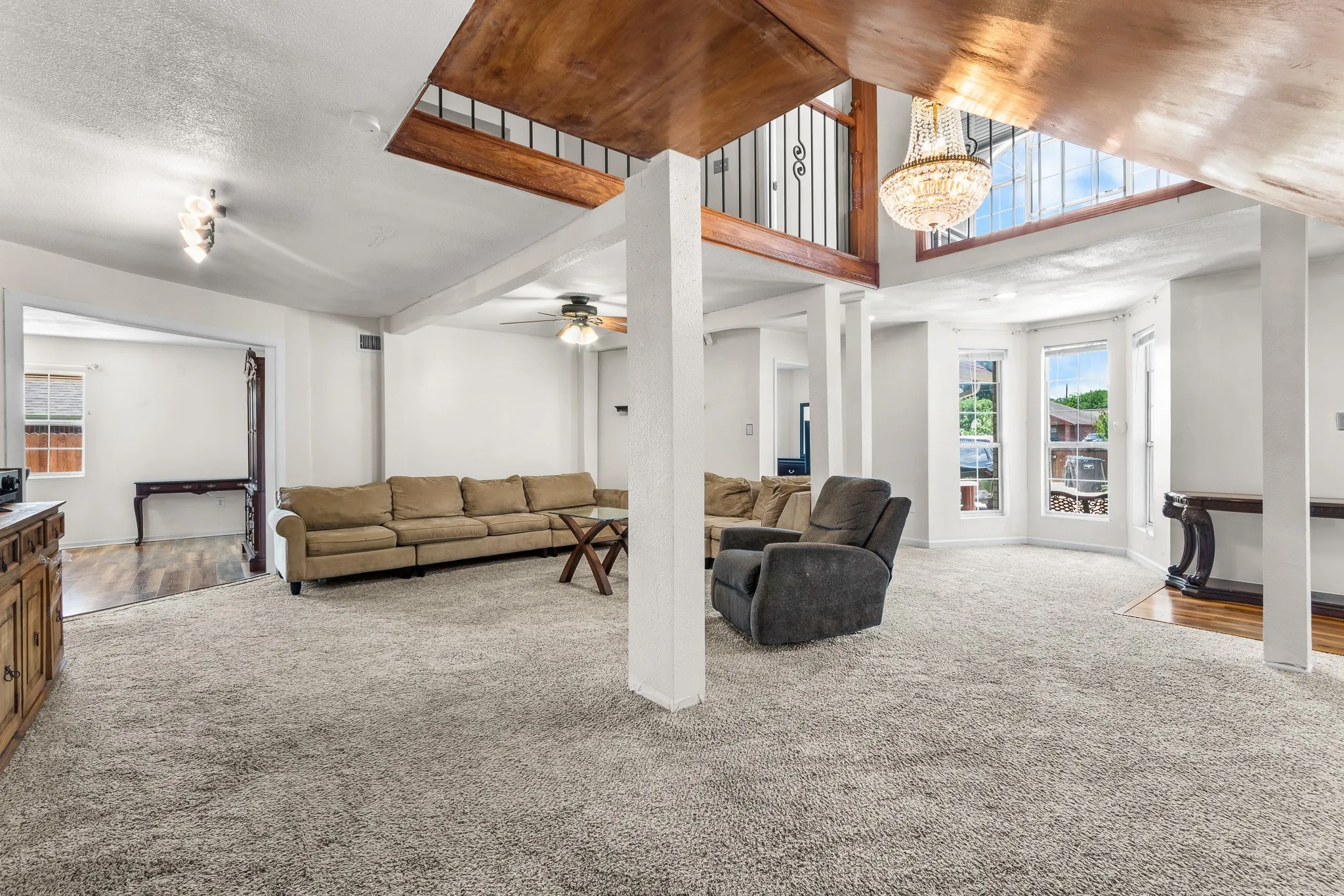 Spacious living area featuring light gray carpeting, a decorative chandelier, and a wood-finish ceiling accent