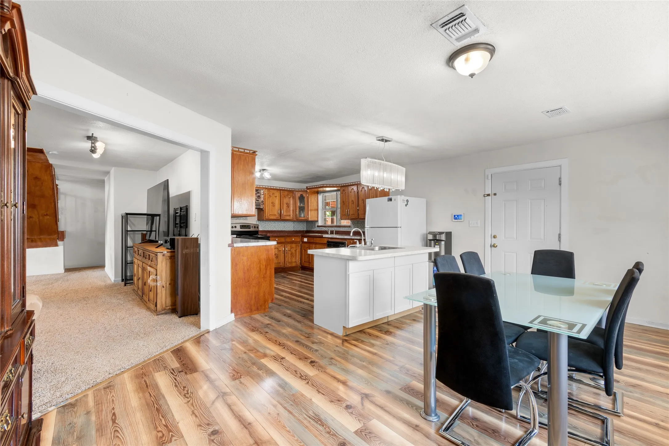 Open-concept kitchen and dining area featuring wood-finish flooring, white cabinetry, a kitchen island with an undermount sink, and recessed lighting