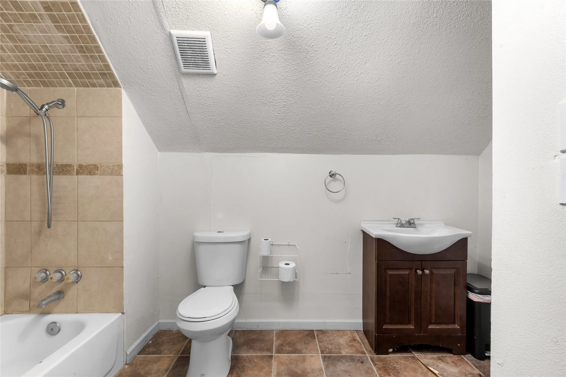 Full bathroom featuring a white bathtub, ceramic tile shower surround with an accent band, white toilet, and a dark wood-finish vanity with an integrated sink