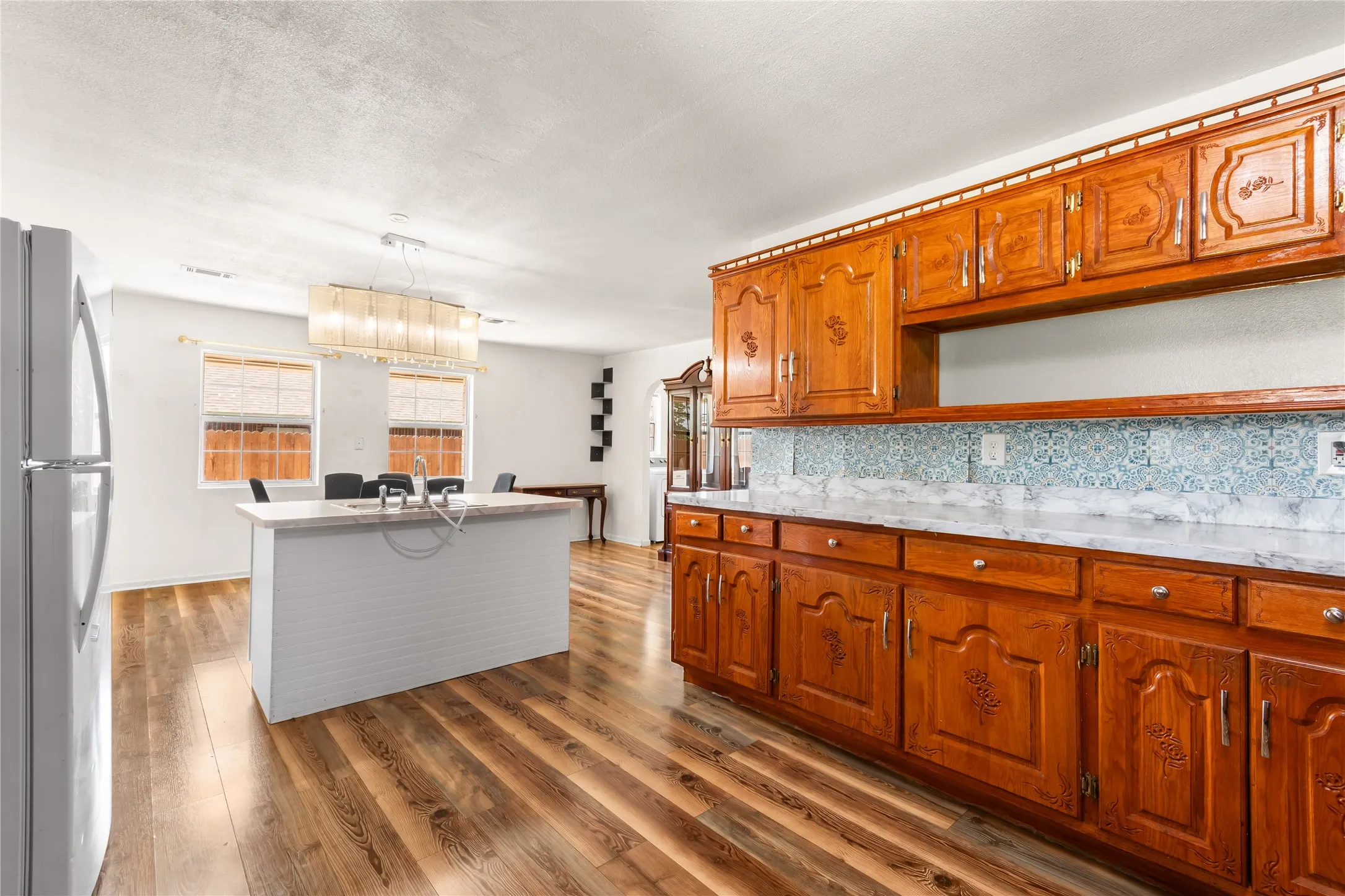 Open-concept kitchen and dining area featuring wood-finish flooring, a white kitchen island with an undermount sink, and traditional wood cabinetry with intricate paneling