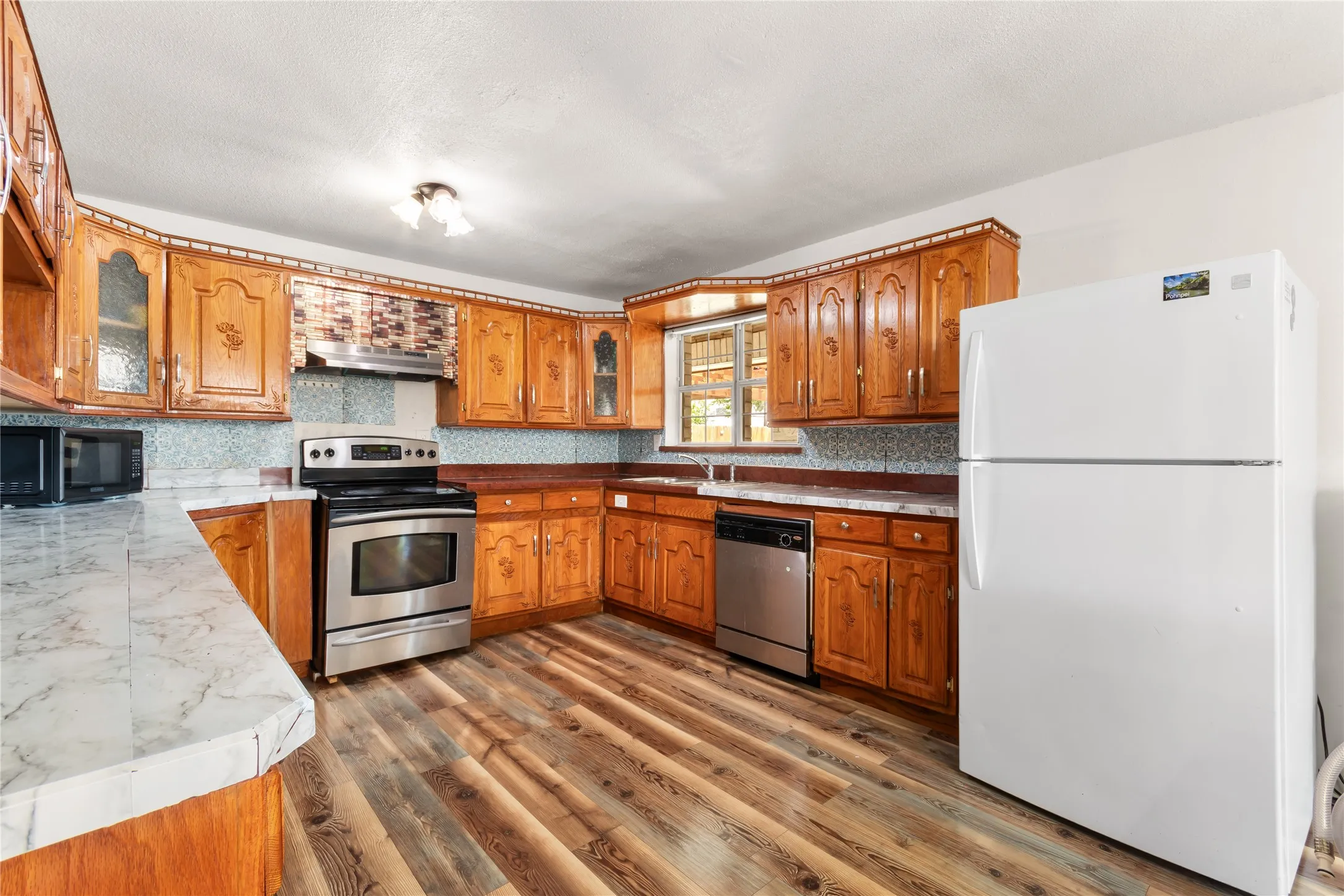 Kitchen featuring wood-finish flooring, oak cabinetry with decorative accents, and a mix of laminate and solid surface countertops
