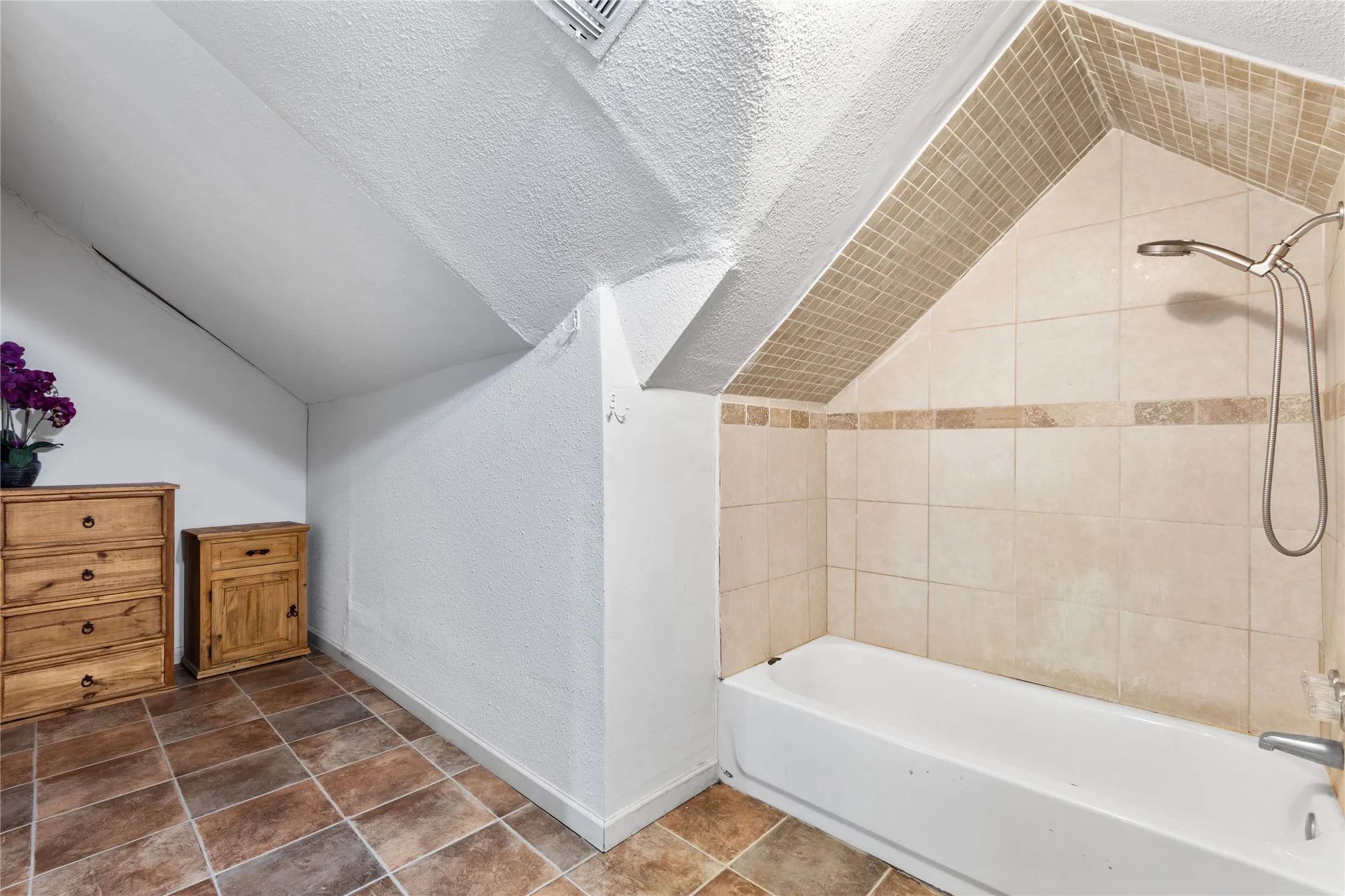 Bathtub with chrome shower fixtures, neutral-toned wall tiles, and accent mosaic tiling