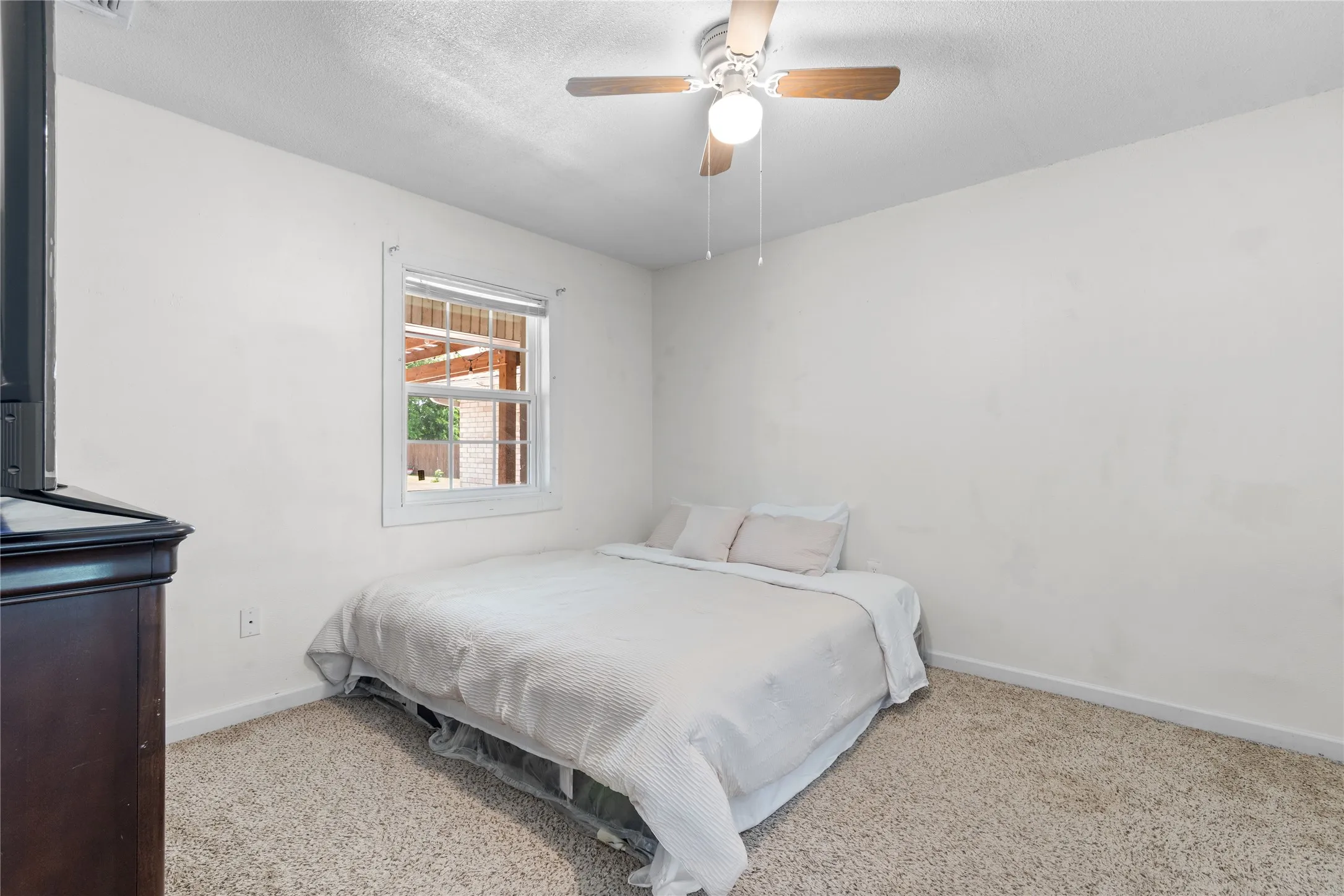 Carpeted room with a ceiling fan, white walls, and a window offering natural light