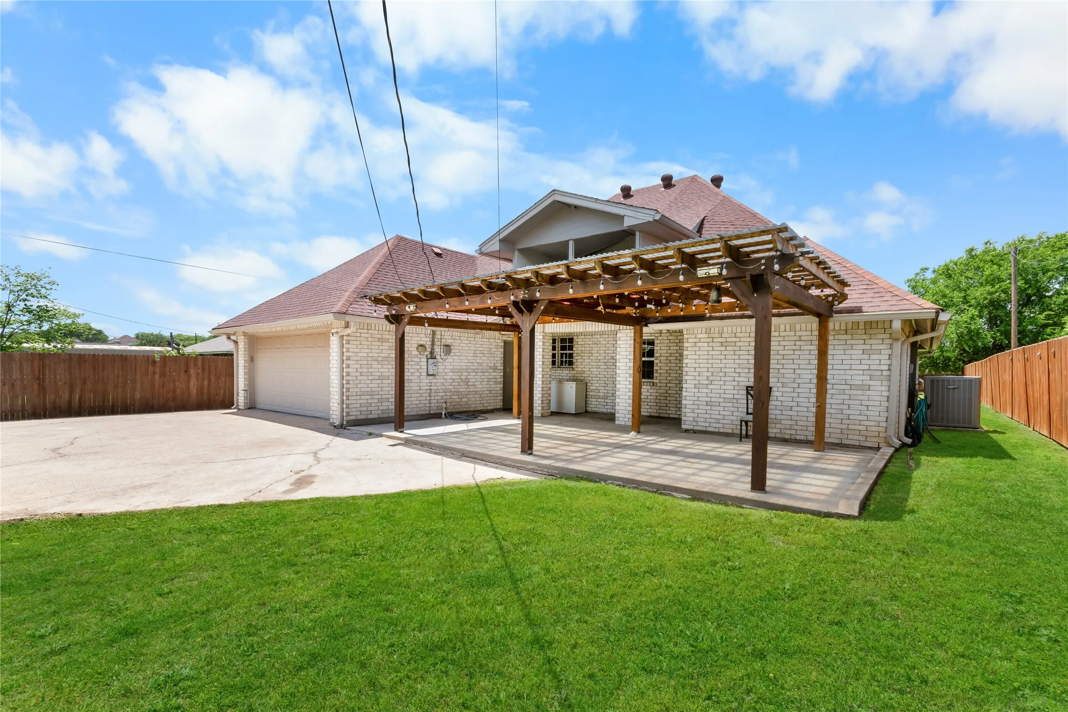 Expansive backyard featuring a manicured lawn, a large paver patio with a wood pergola, and a detached two-car garage
