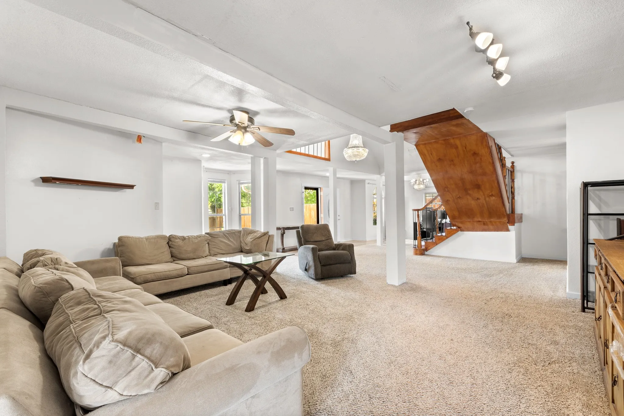Spacious interior featuring a prominent wood staircase, carpeted flooring, white walls, and a ceiling fan