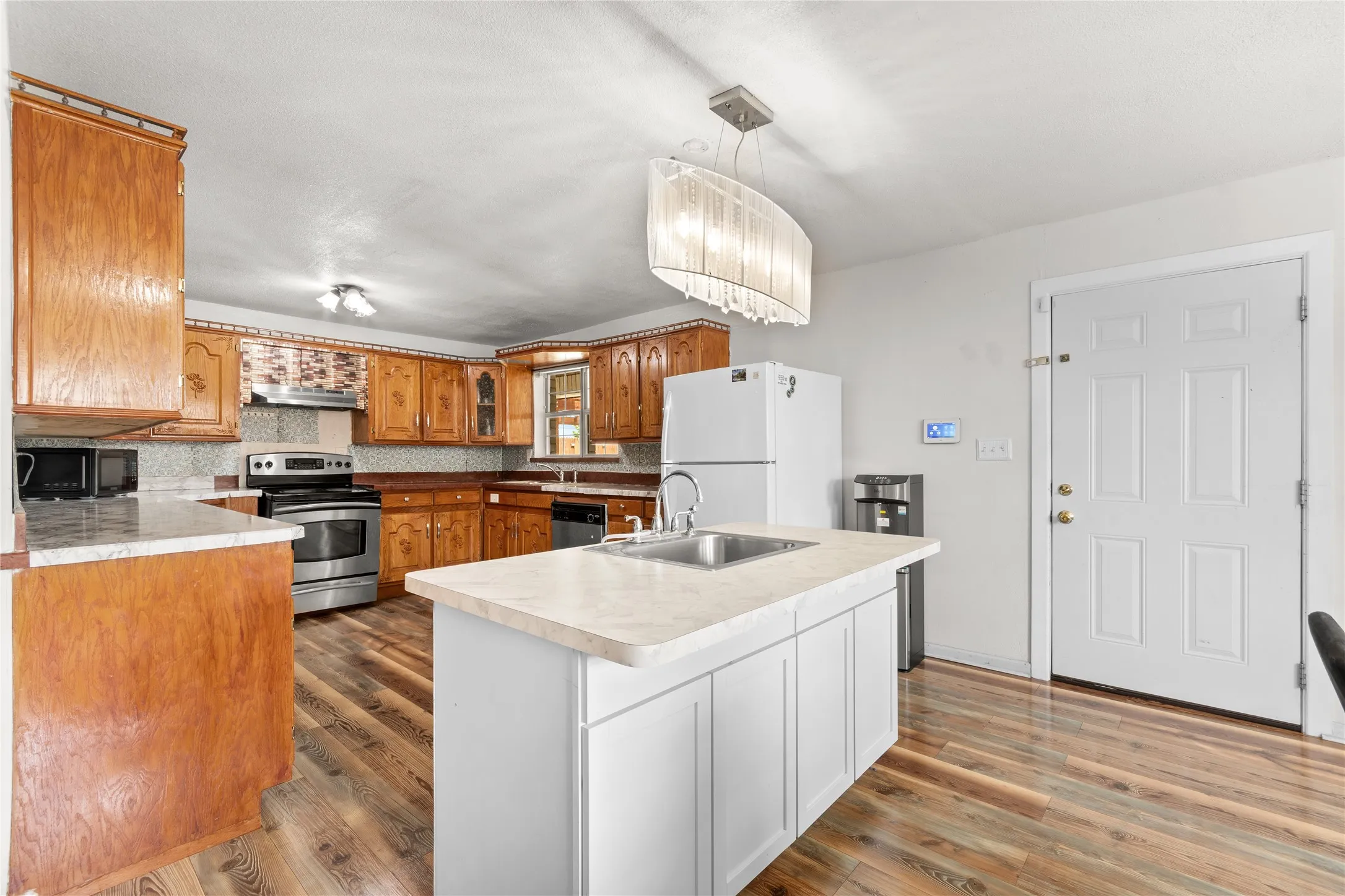 Kitchen featuring a center island with integrated sink, wood-finish flooring, and a stainless steel appliance suite including a range and dishwasher