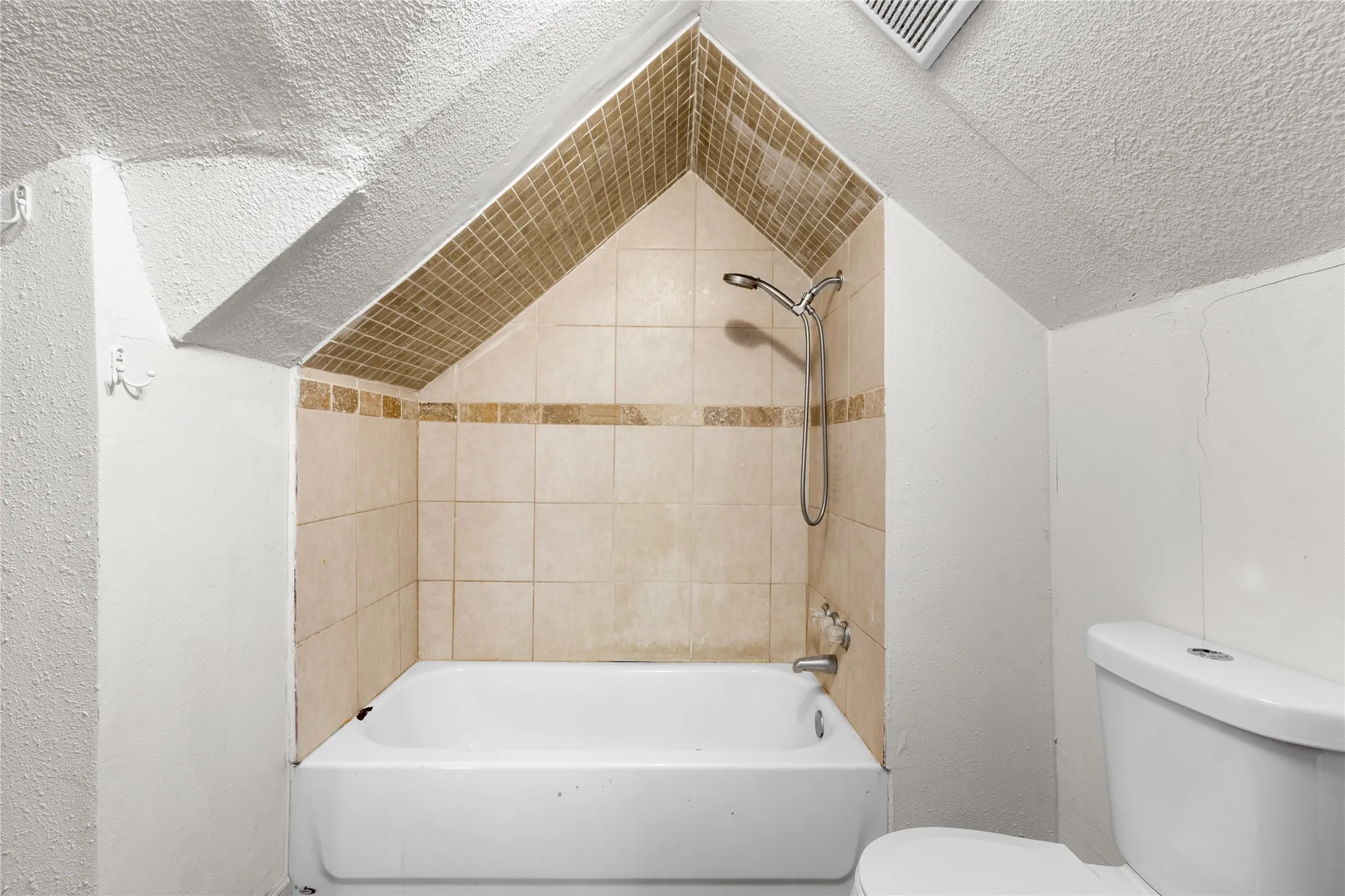 Bathtub with light-toned tiled surround, decorative accent strip, and a handheld showerhead