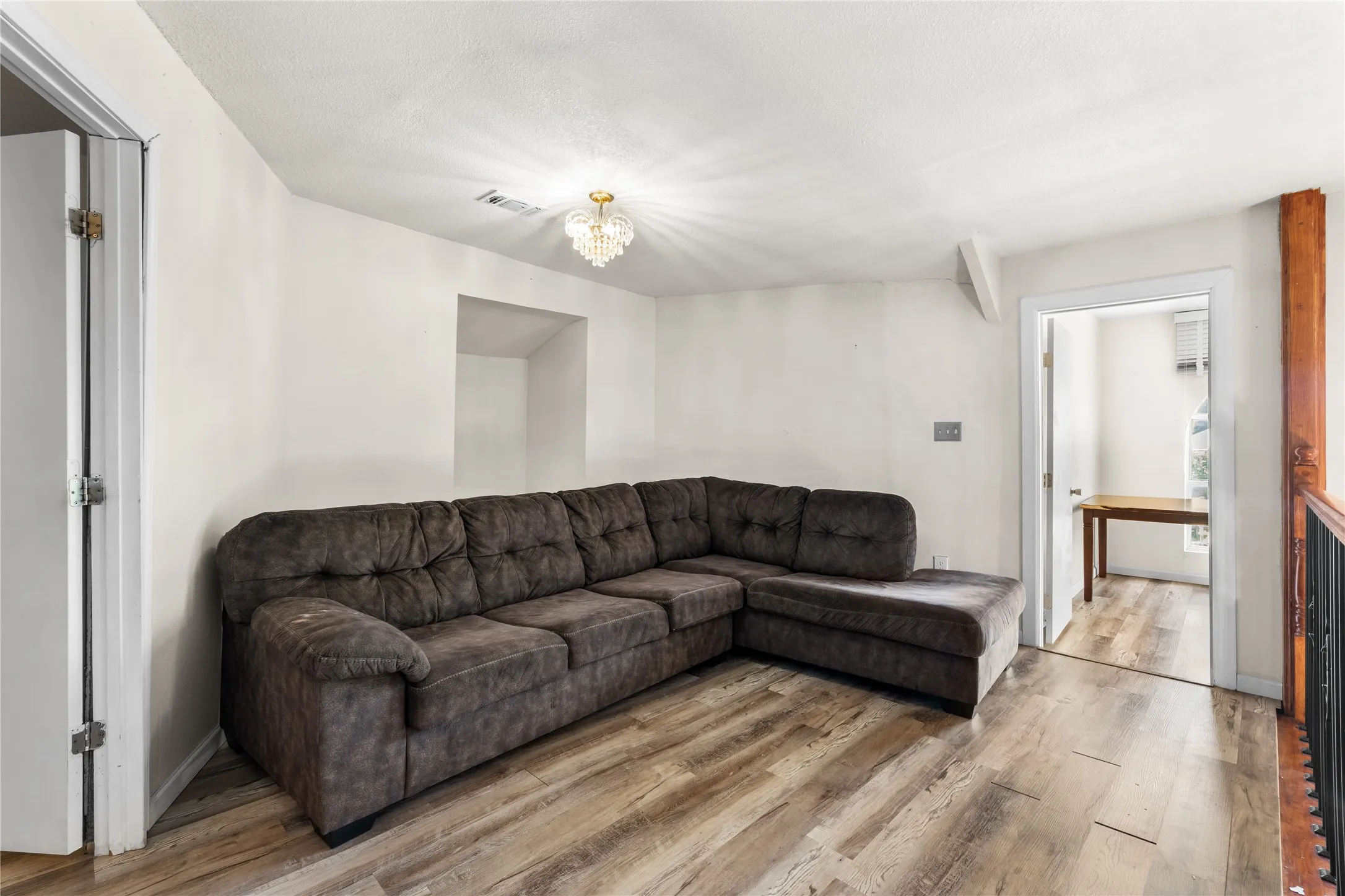 Spacious room featuring wood-finish flooring, white walls, and a decorative ceiling light fixture