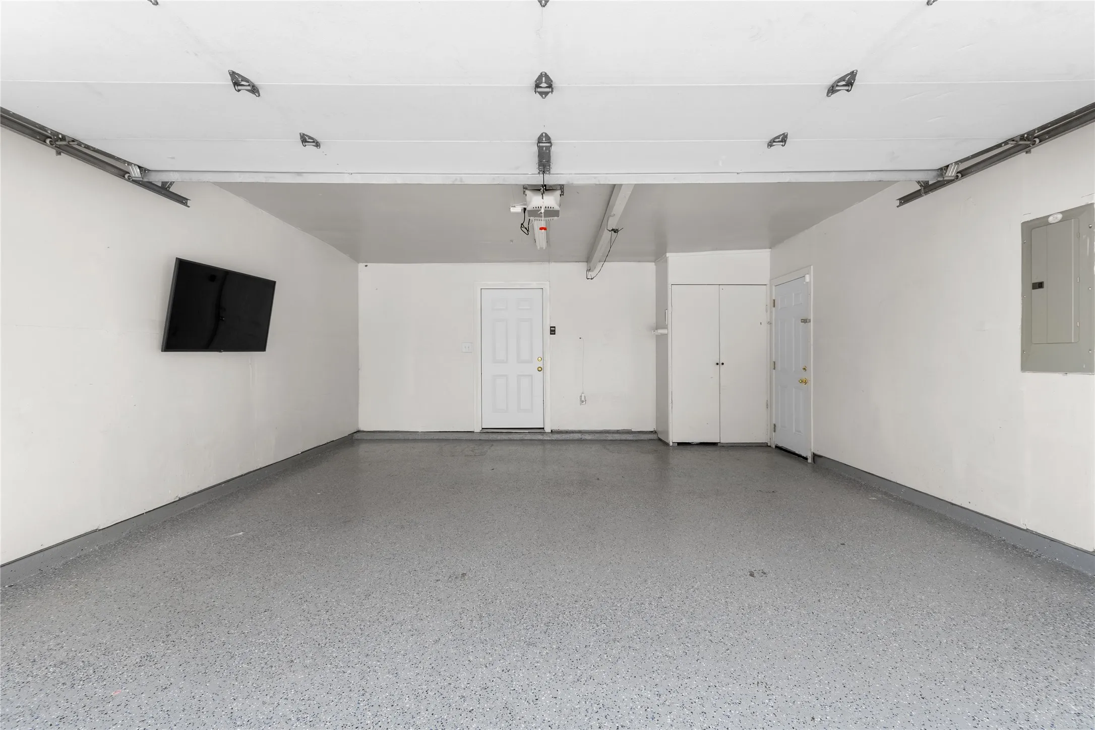 Spacious 2-car attached garage featuring a durable epoxy-coated floor, painted walls, an overhead garage door mechanism, an interior access door, and built-in white storage cabinetry