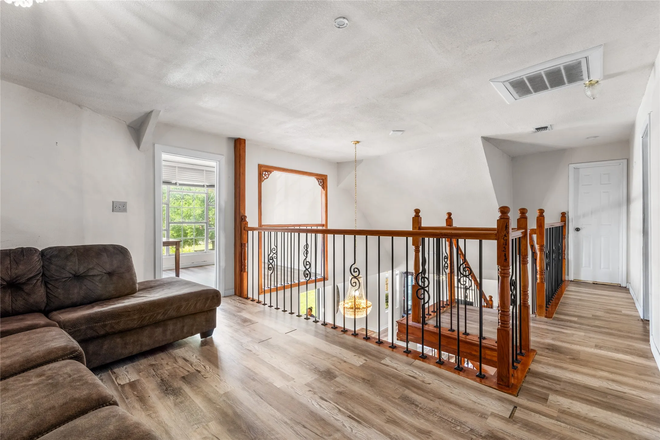 Upper-level landing featuring wood-finish flooring, white walls, and a wood and wrought iron staircase railing
