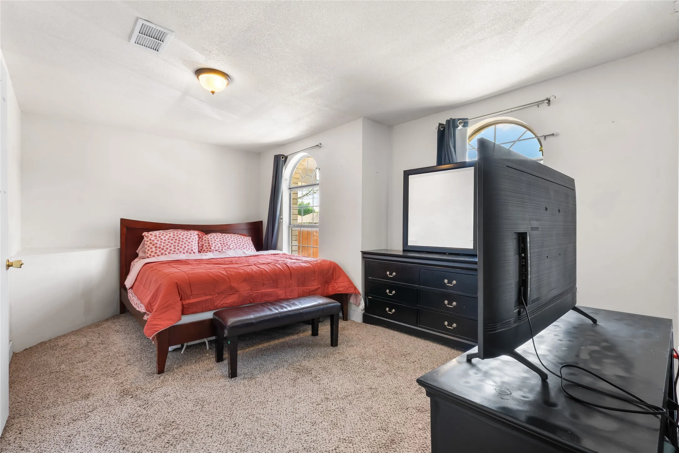 Carpeted bedroom featuring two arched windows, a flush-mount ceiling light, and white painted walls