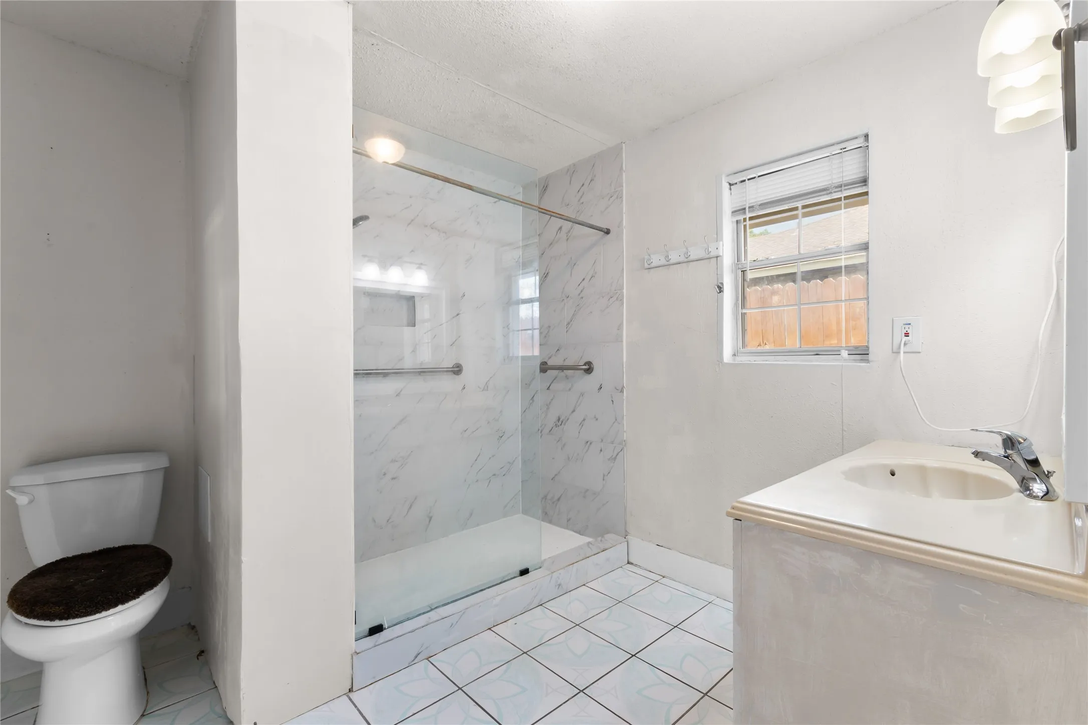 Bathroom featuring a glass-enclosed shower with white marble-look paneling, a single vanity with an integrated sink, and white tile flooring