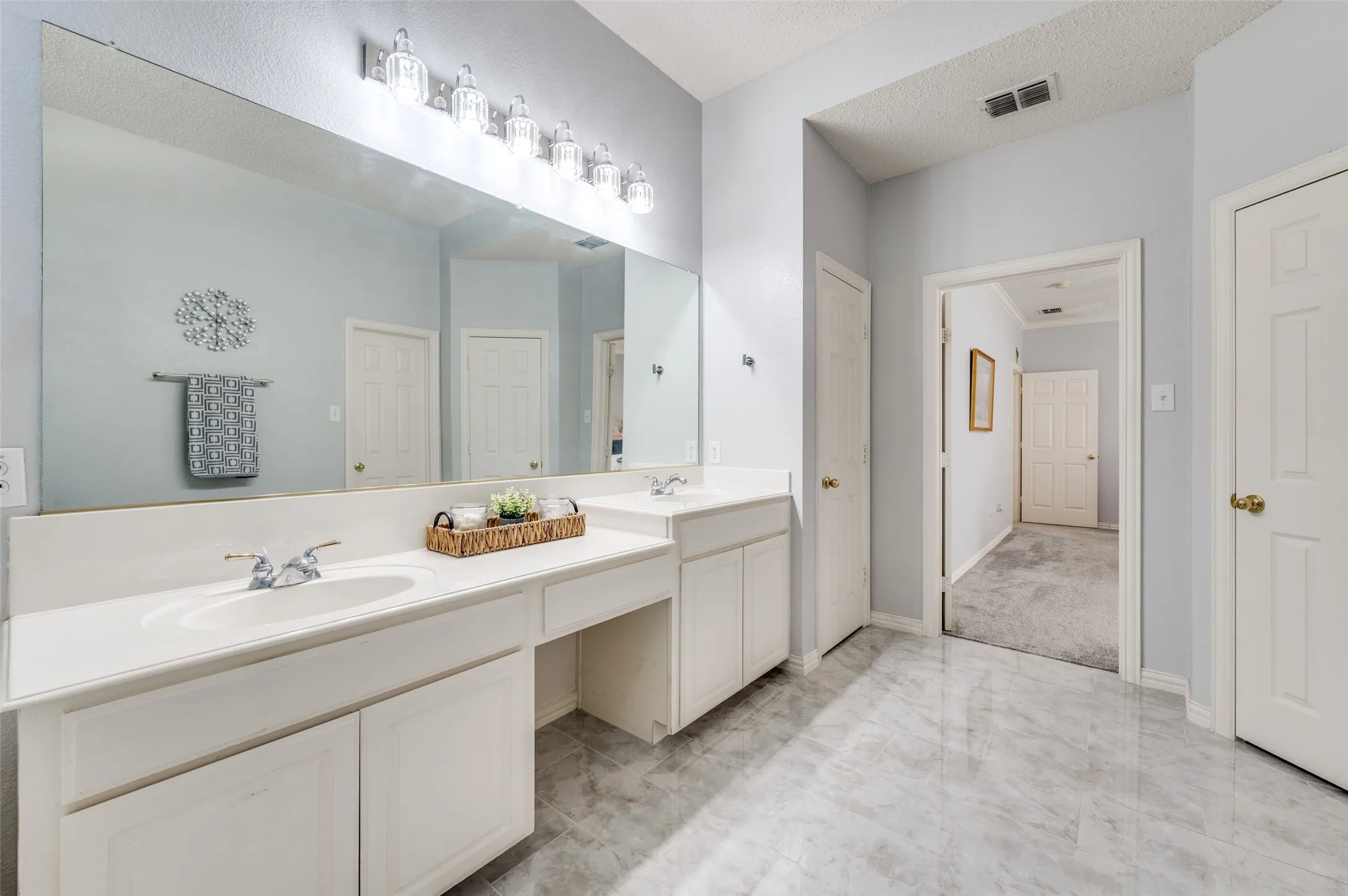 Dual vanity with integrated sinks, expansive mirror, dedicated vanity seating area, white cabinetry, and a tiled floor