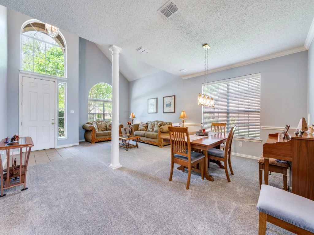 Spacious interior featuring vaulted ceilings, a prominent decorative column, and a combination of carpet and tile entry flooring.