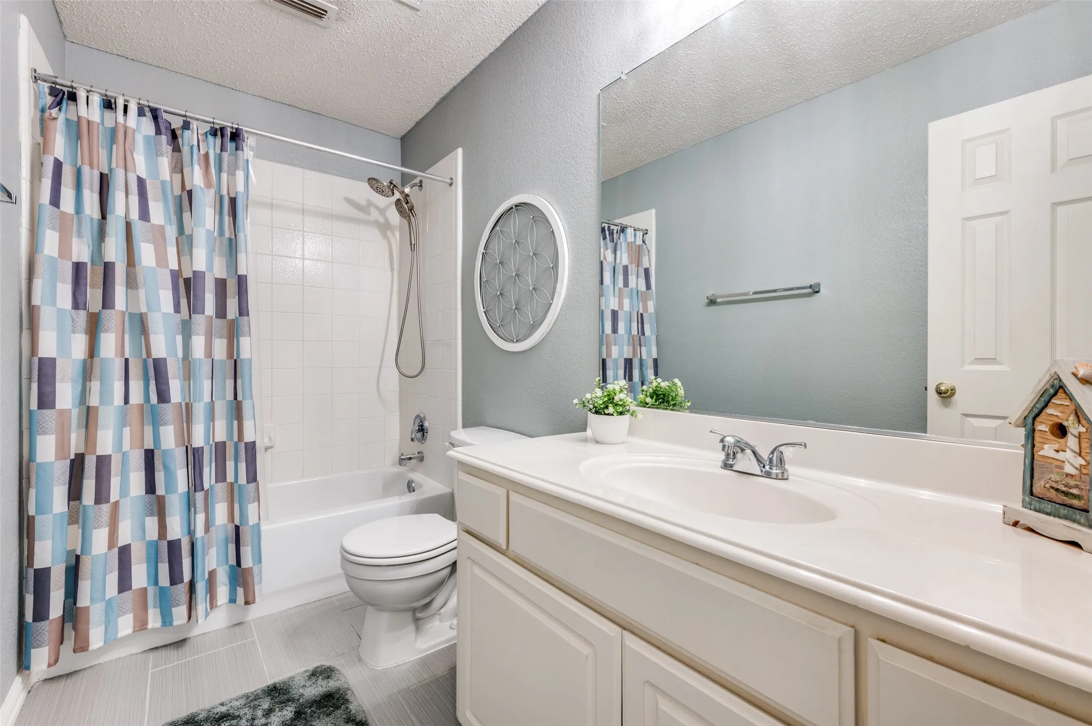 Bathroom featuring a built-in vanity with integrated sink, chrome faucet, full-width mirror, a shower-tub combination with tile surround, and light gray tile flooring