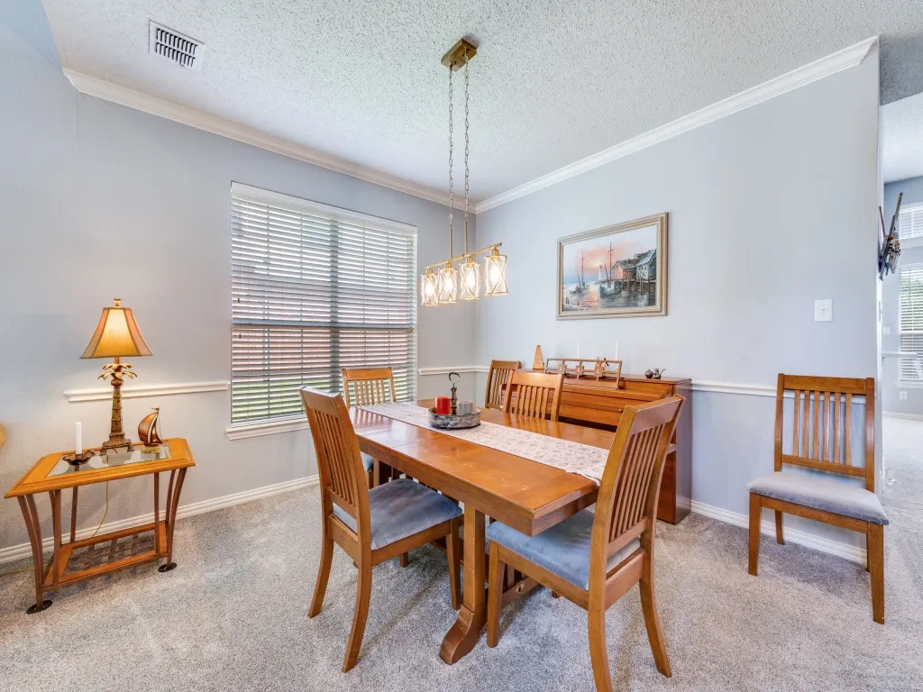 Dining area featuring light gray wall paint with white wainscoting and crown molding and decorative lighting.