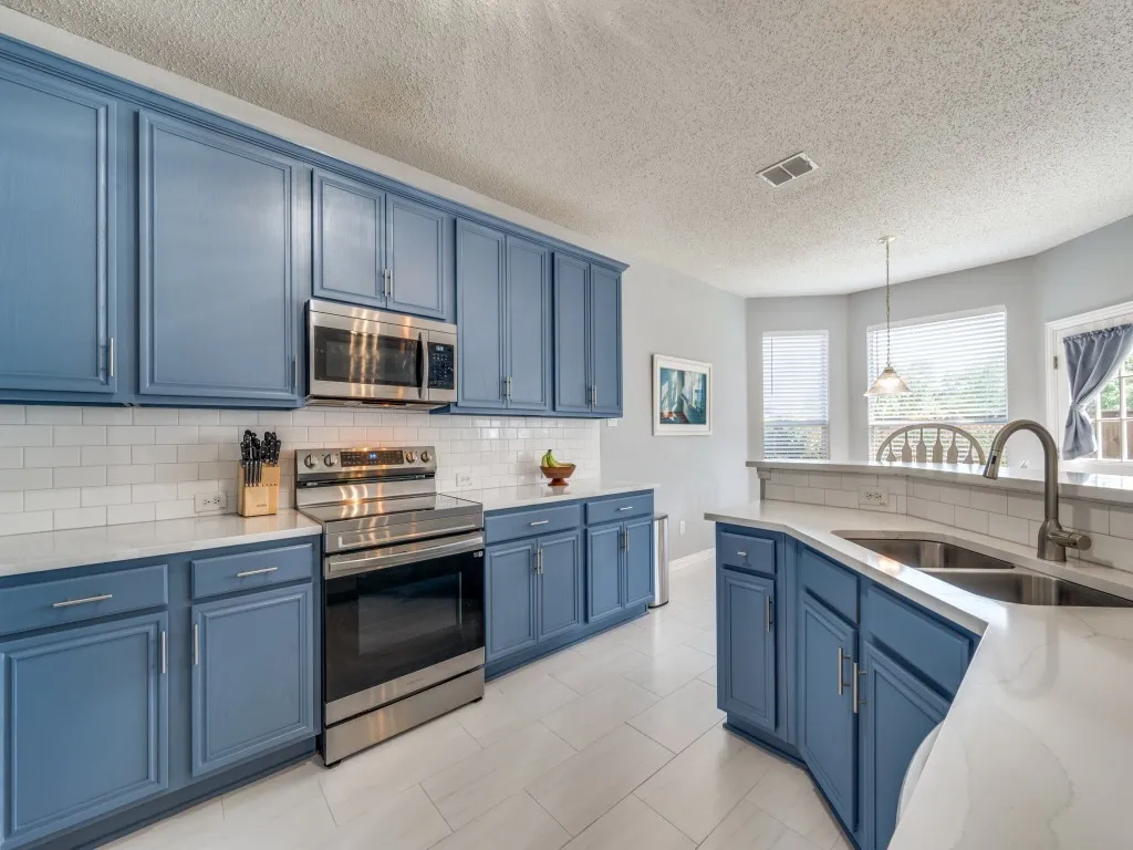 Kitchen featuring blue cabinetry, stainless steel appliances, a white subway tile backsplash, white Quartz countertops, and light-toned tile flooring