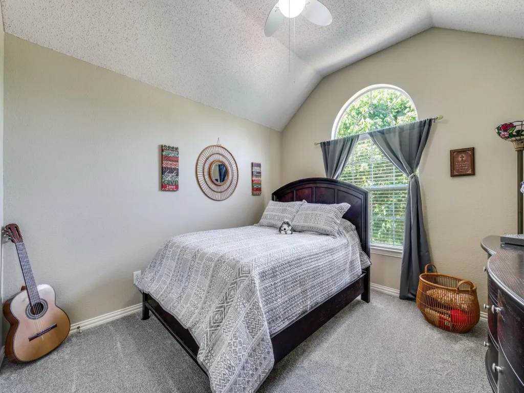 Upstairs bedroom #1 featuring vaulted ceiling, a large arched window, and neutral wall tones