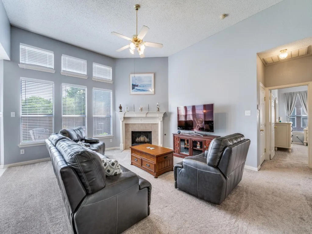 Living area featuring high ceilings, light-hued carpeting, and ceiling fan with 2" blinds covering many windows.