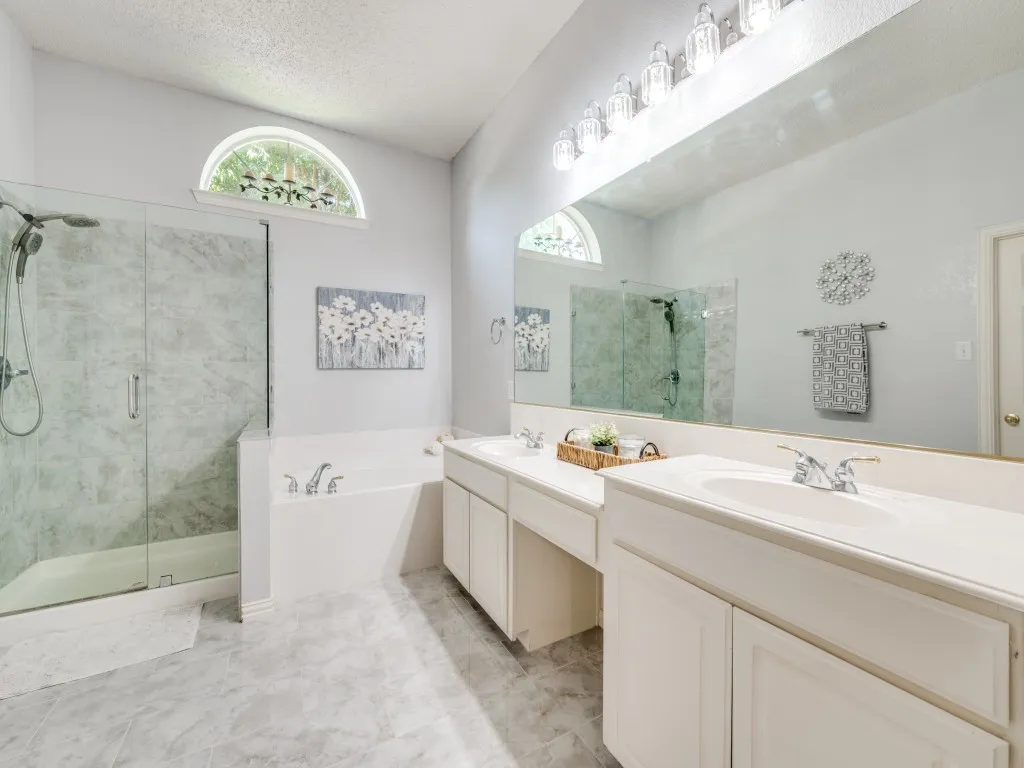 Ensuite bath featuring a glass-enclosed shower with updated glass enclosure, a built-in garden tub, dual vanity with stone type countertops, a large mirror, and an arched transom window