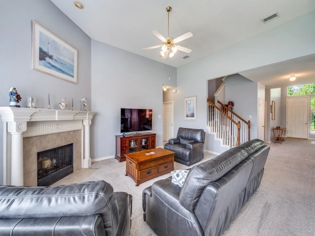 Living area featuring a floor-to-ceiling fireplace with mantel, vaulted ceilings, and a ceiling fan with integrated lighting