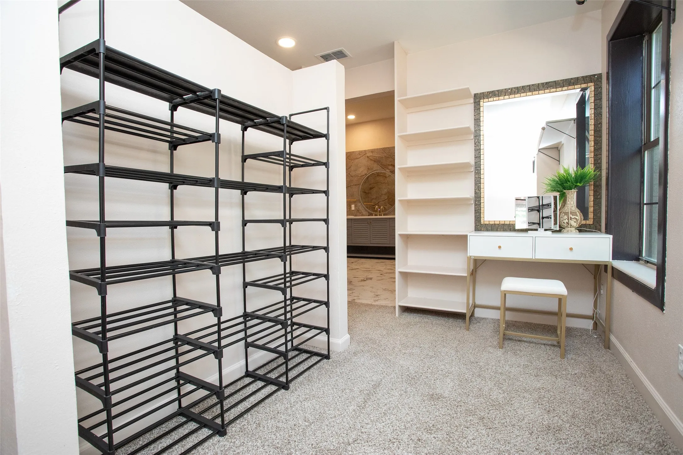 The adjoining dressing area includes generous storage, open shelving, and space for a vanity or dressing station, creating a functional and well-appointed extension of the primary suite.