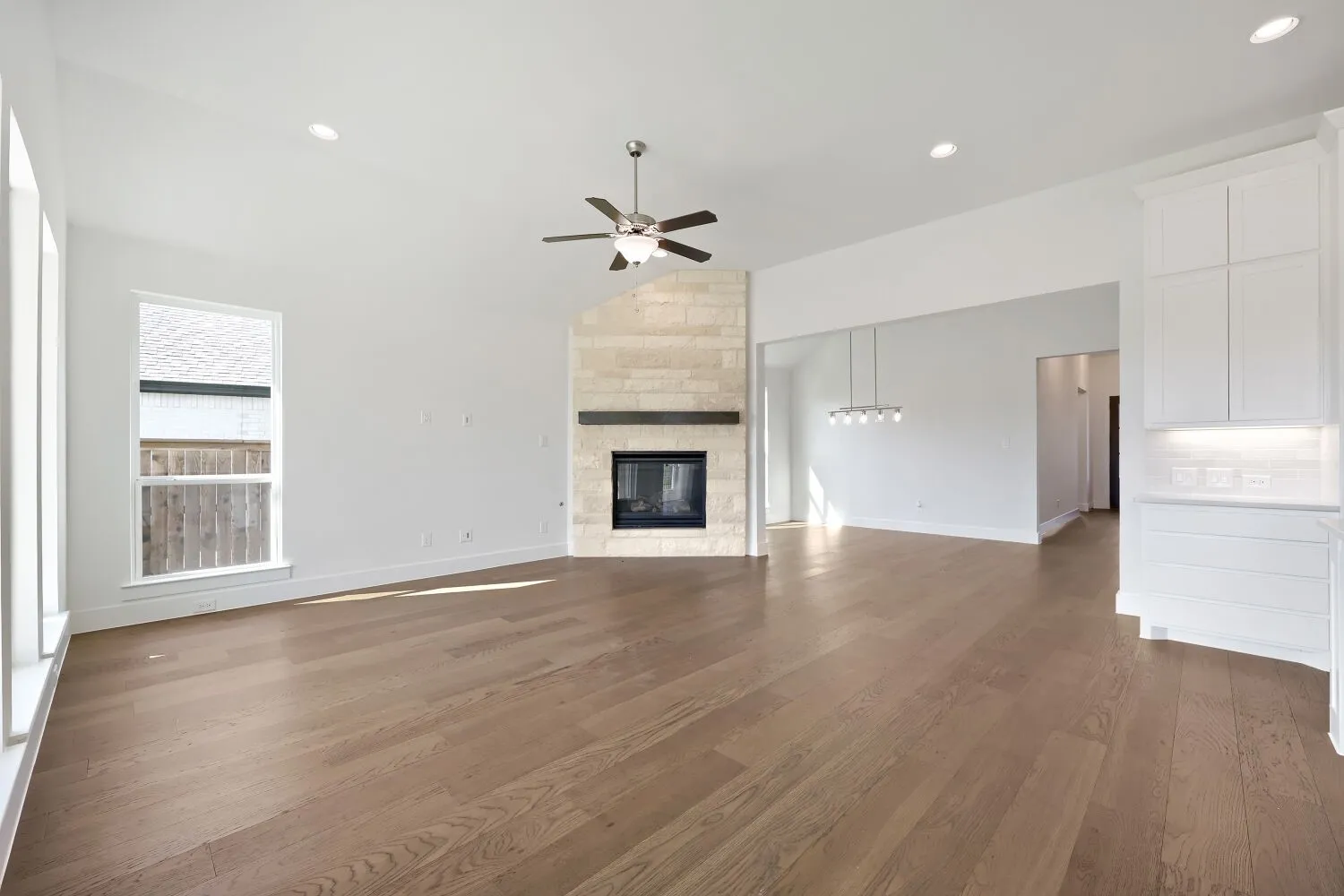 Spacious room with wood-finish flooring, a stone-clad fireplace with a dark mantel, multiple windows, and recessed lighting