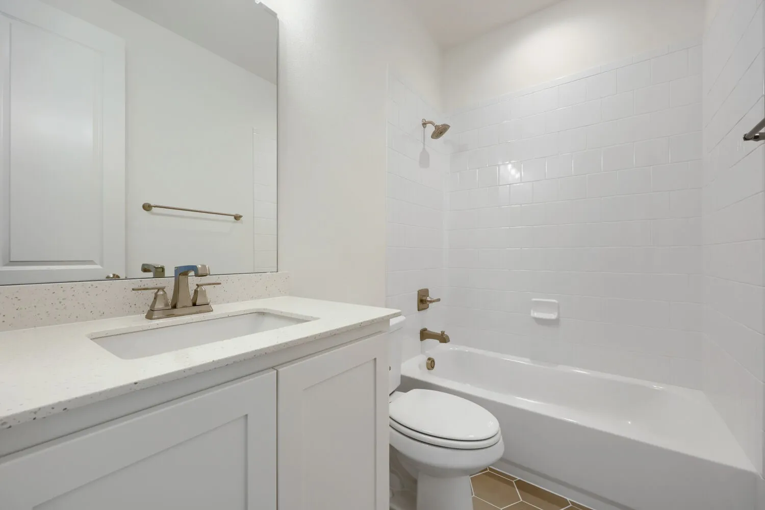 Bathroom featuring a white vanity with an integrated sink, a speckled countertop, brushed nickel fixtures, a tub with subway tile surround, and hexagonal floor tiling