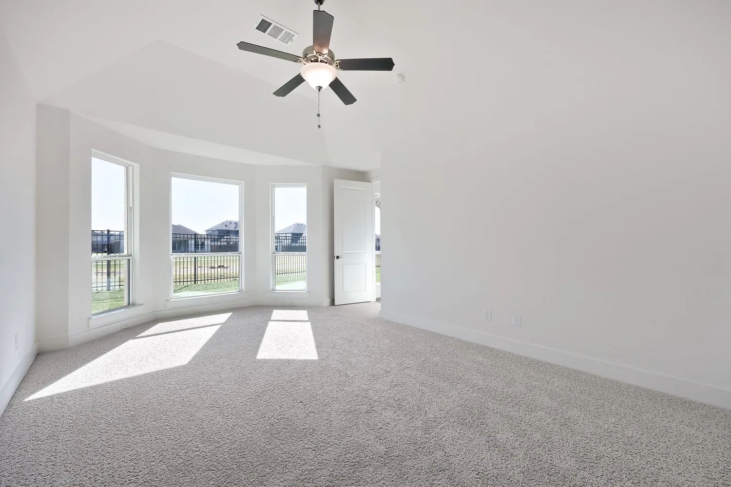 Carpeted room featuring a bay window, vaulted ceiling, and a ceiling fan with light fixture