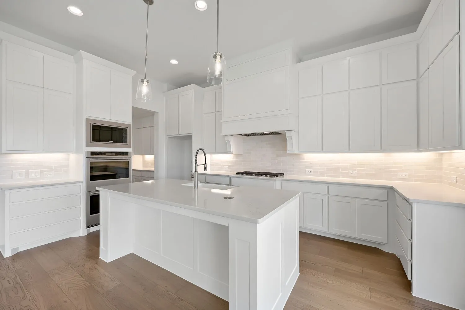 Kitchen featuring white cabinetry, light countertops, wood-finish flooring, stainless steel appliances, and an island with a sink