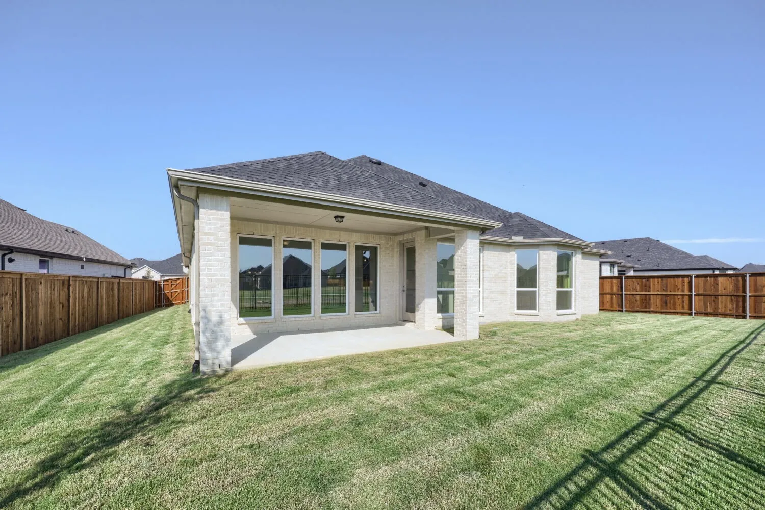Expansive backyard featuring a manicured lawn, full privacy fencing, a covered patio, and multiple large windows
