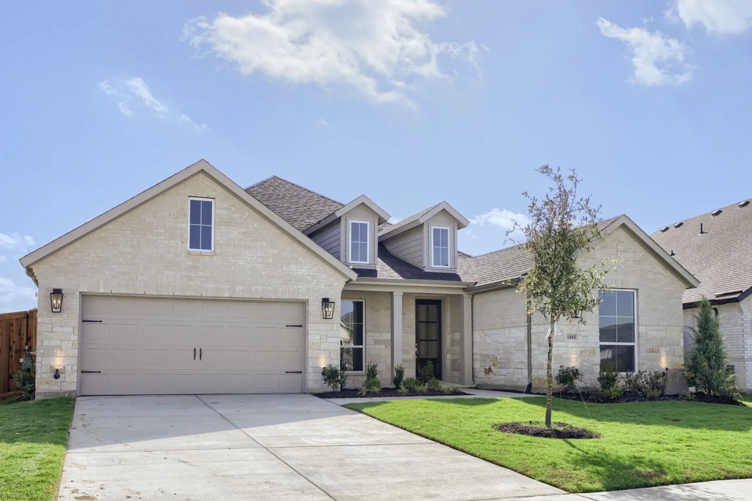 Stone and brick exterior with a two-car garage, dormer windows, and a landscaped front yard