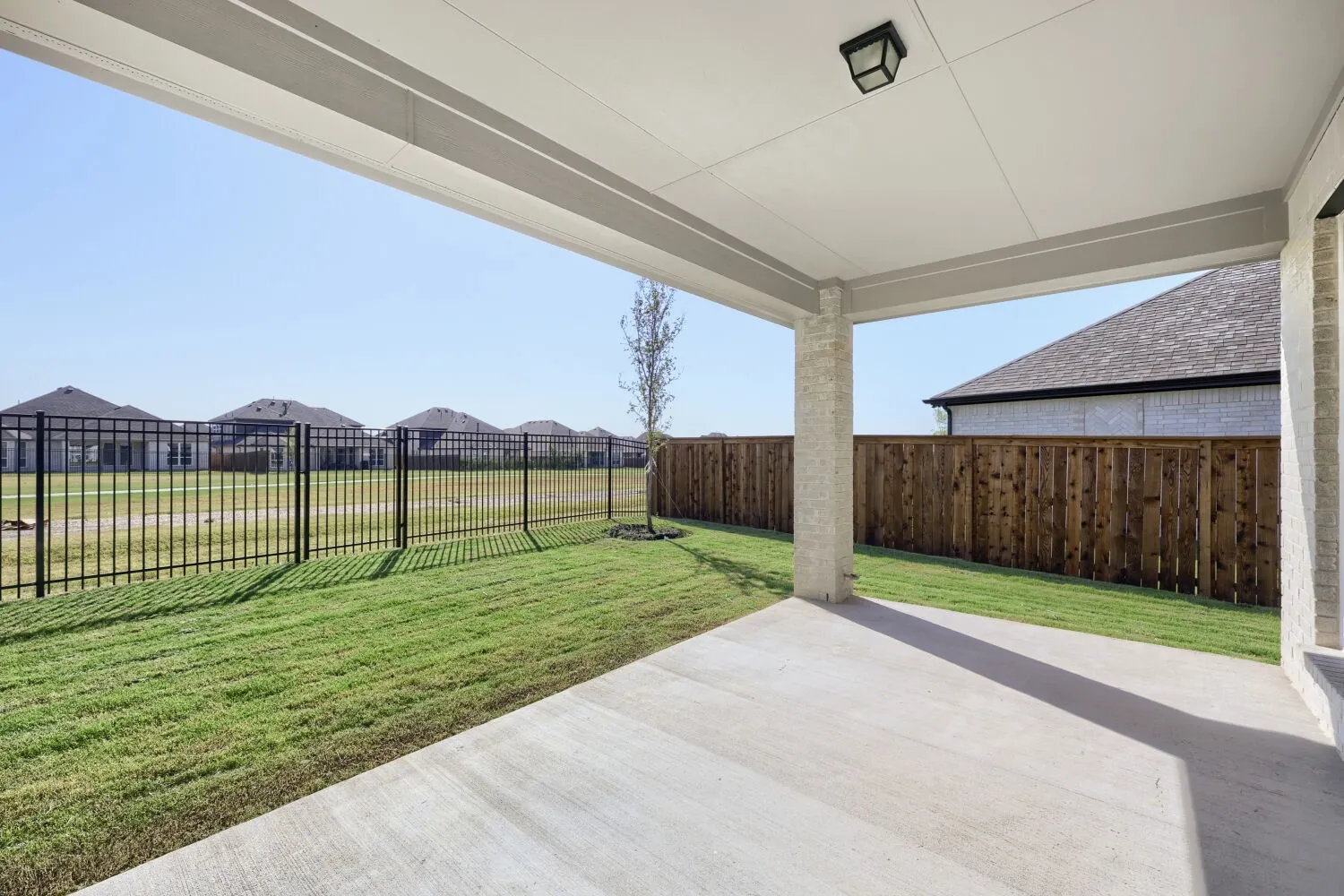 Covered patio with concrete flooring, stone-clad columns, and a flush-mount ceiling light