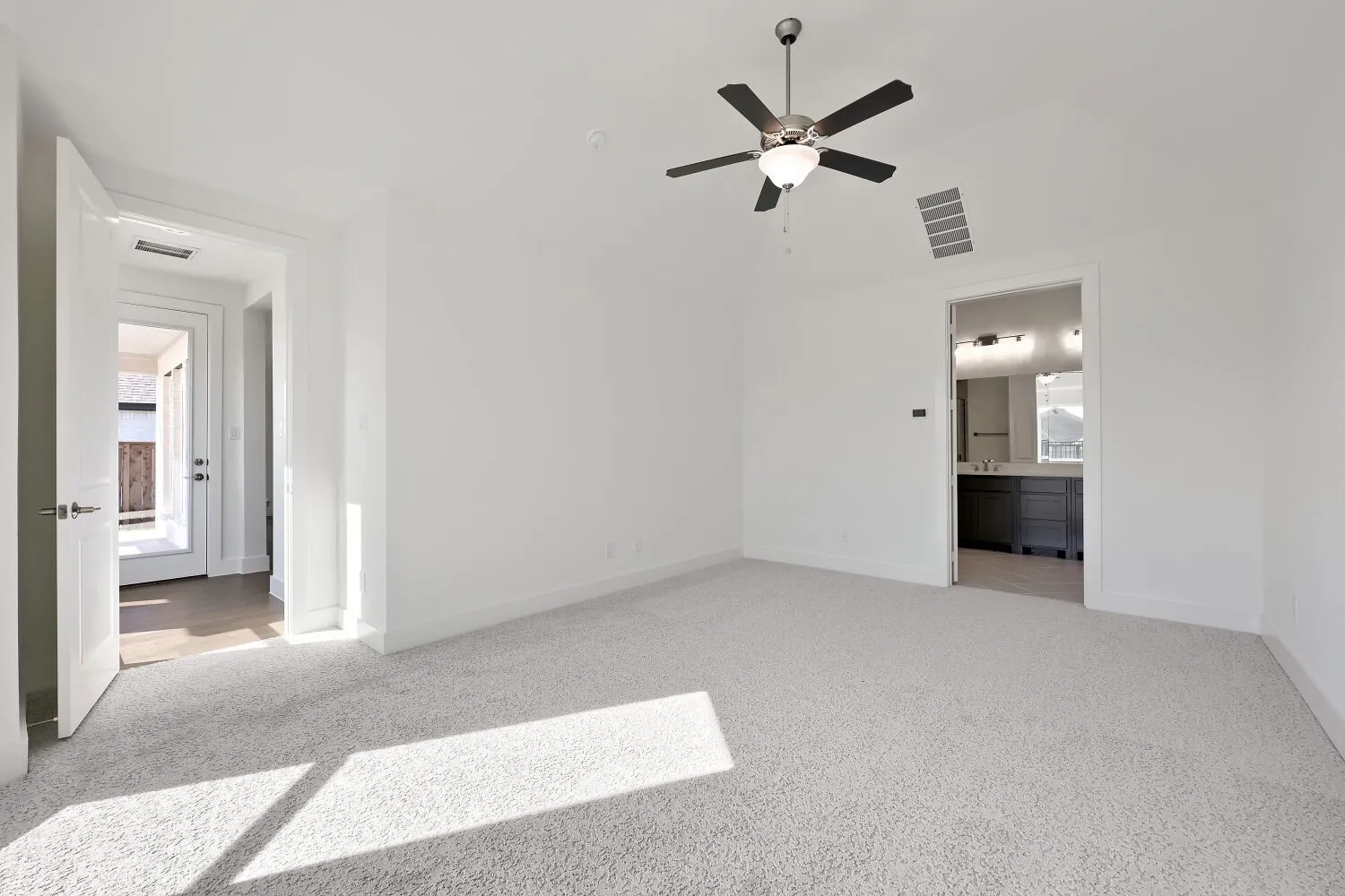 Vaulted ceiling room with light-toned carpeting and an overhead fan