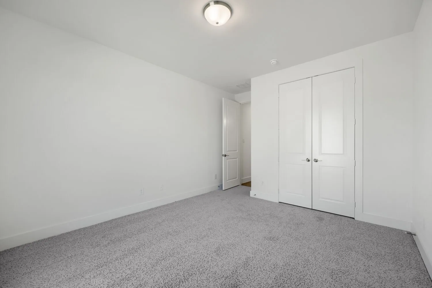 Neutral wall paint with gray carpeting, featuring a flush mount ceiling light and white bi-fold closet doors