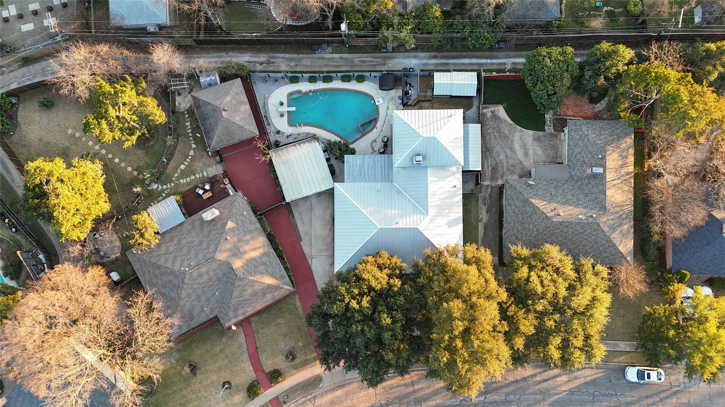 The property features a private swimming pool with a diving board, a spacious red paved driveway, and a well-maintained lawn with mature trees