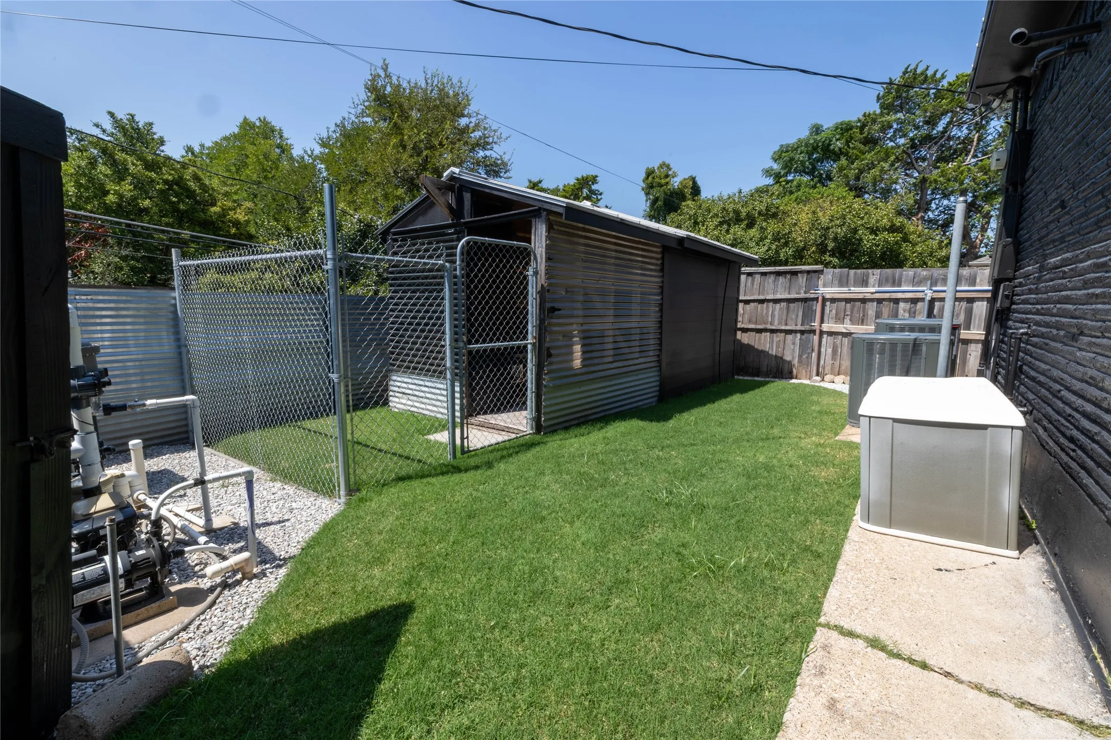 Manicured lawn area featuring a corrugated metal shed, chain-link fencing, and a gravel-covered utility zone