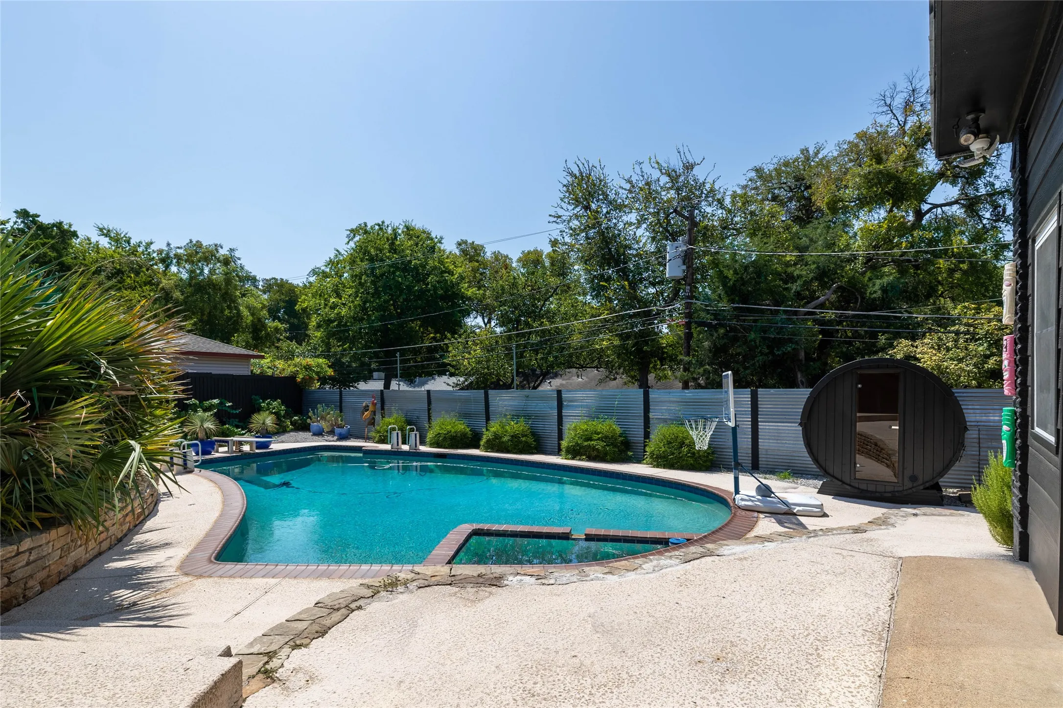 Curved swimming pool with an integrated spa, surrounded by an exposed aggregate concrete patio