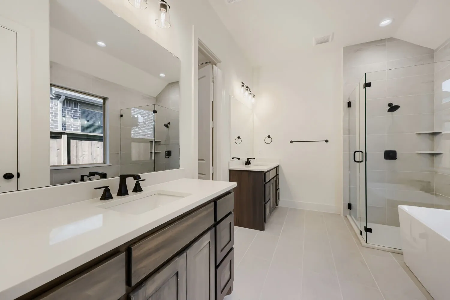 Dual vanities with white countertops, matte black fixtures, a glass-enclosed shower with tile surround, and a separate soaking tub