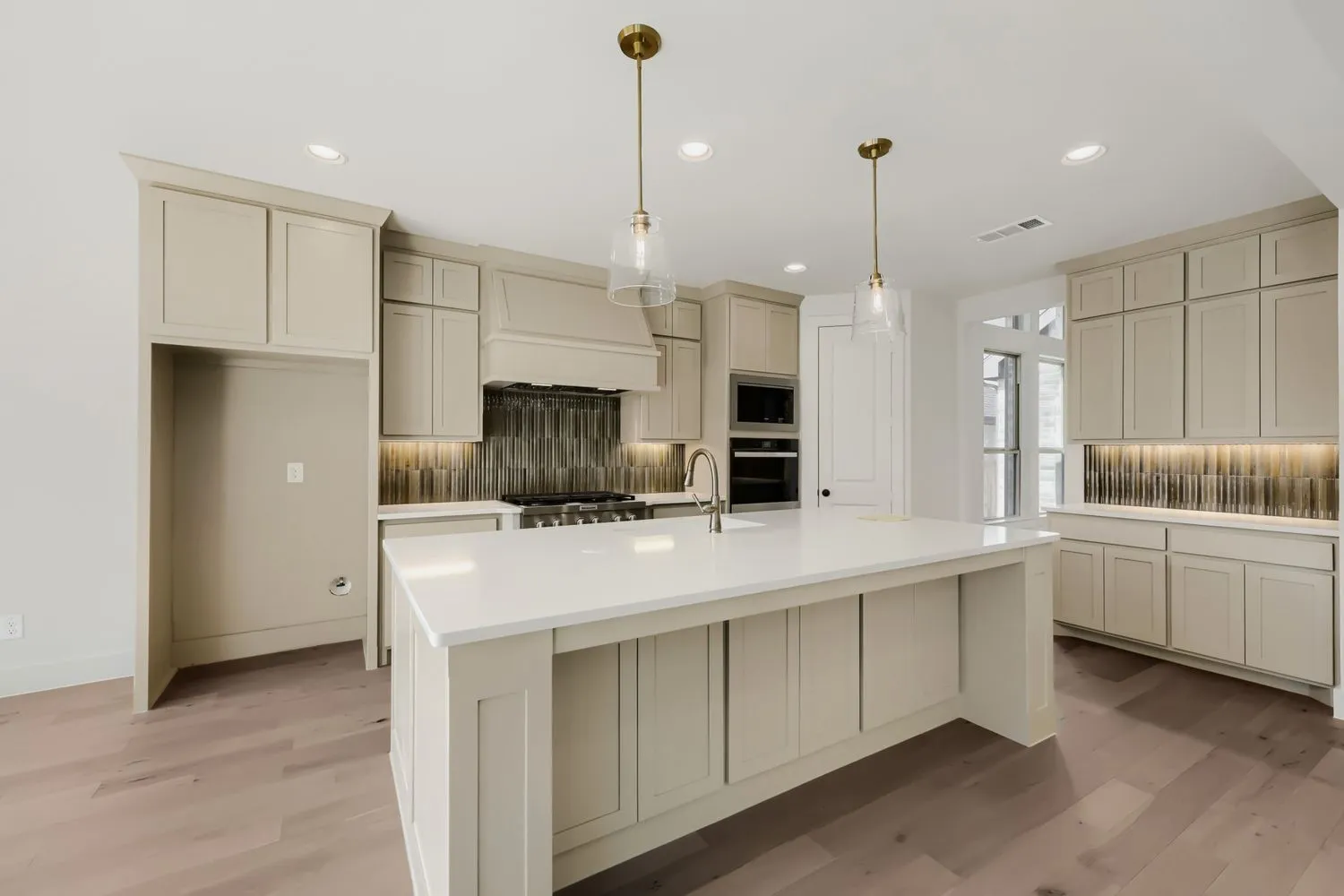 Kitchen featuring a large central island with a sink, white countertops, built-in stainless steel appliances, and wood-finish flooring