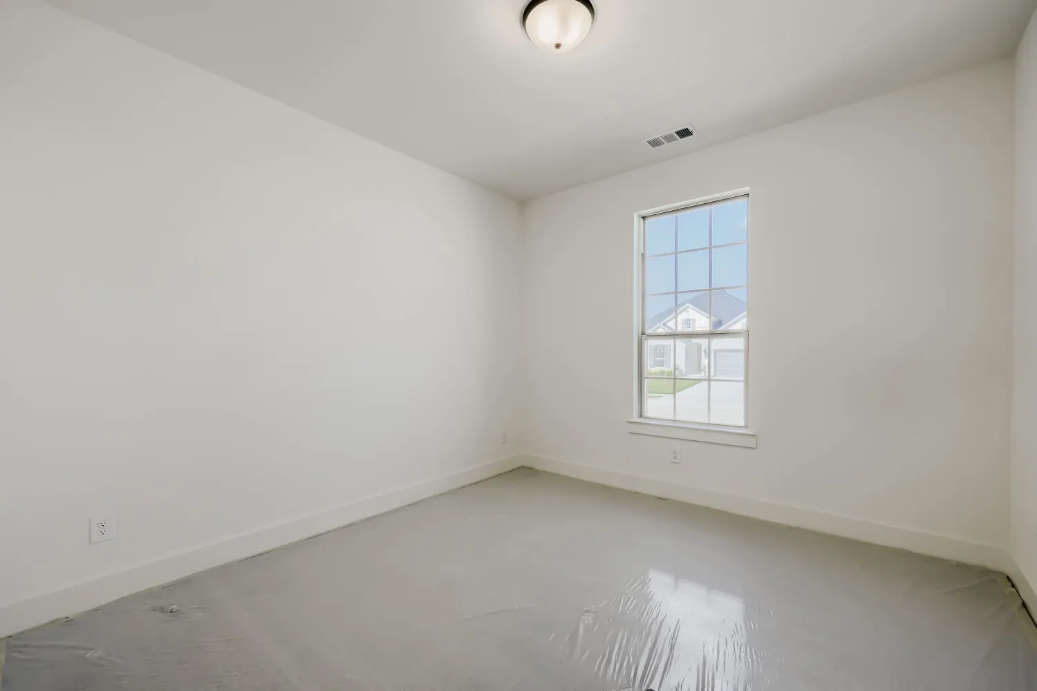 Neutral wall color, single window with grid pattern, overhead flush mount light fixture, ceiling vent, protective floor covering