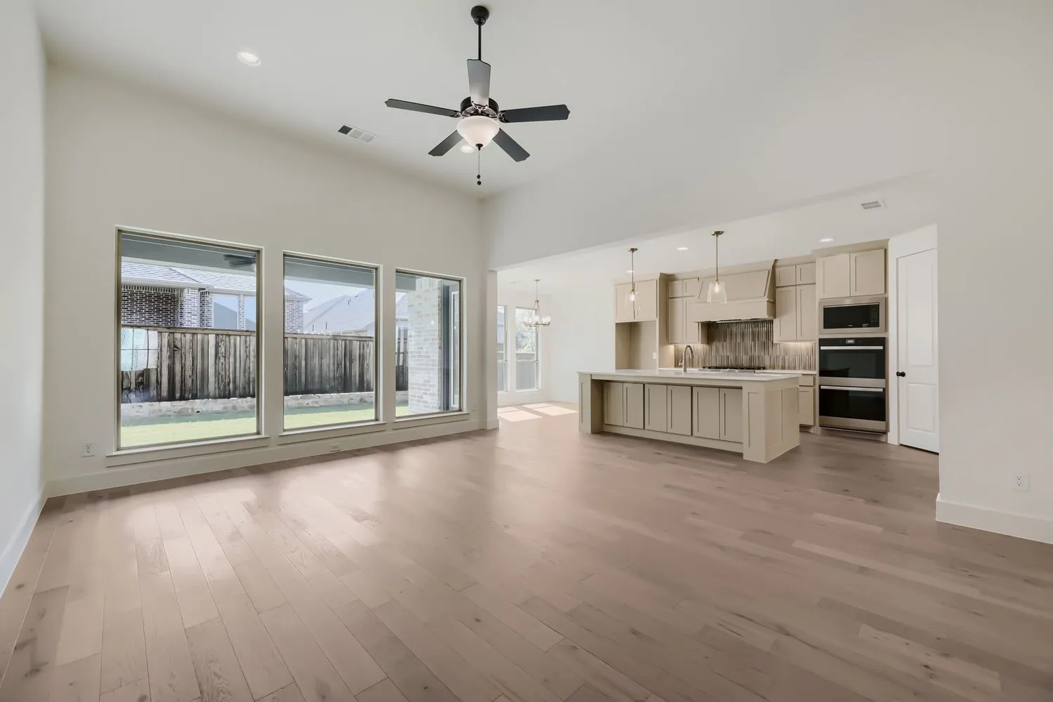 Vaulted ceiling with a ceiling fan, wood-finish flooring, a kitchen island with built-in cabinetry, stainless steel double ovens, and large windows