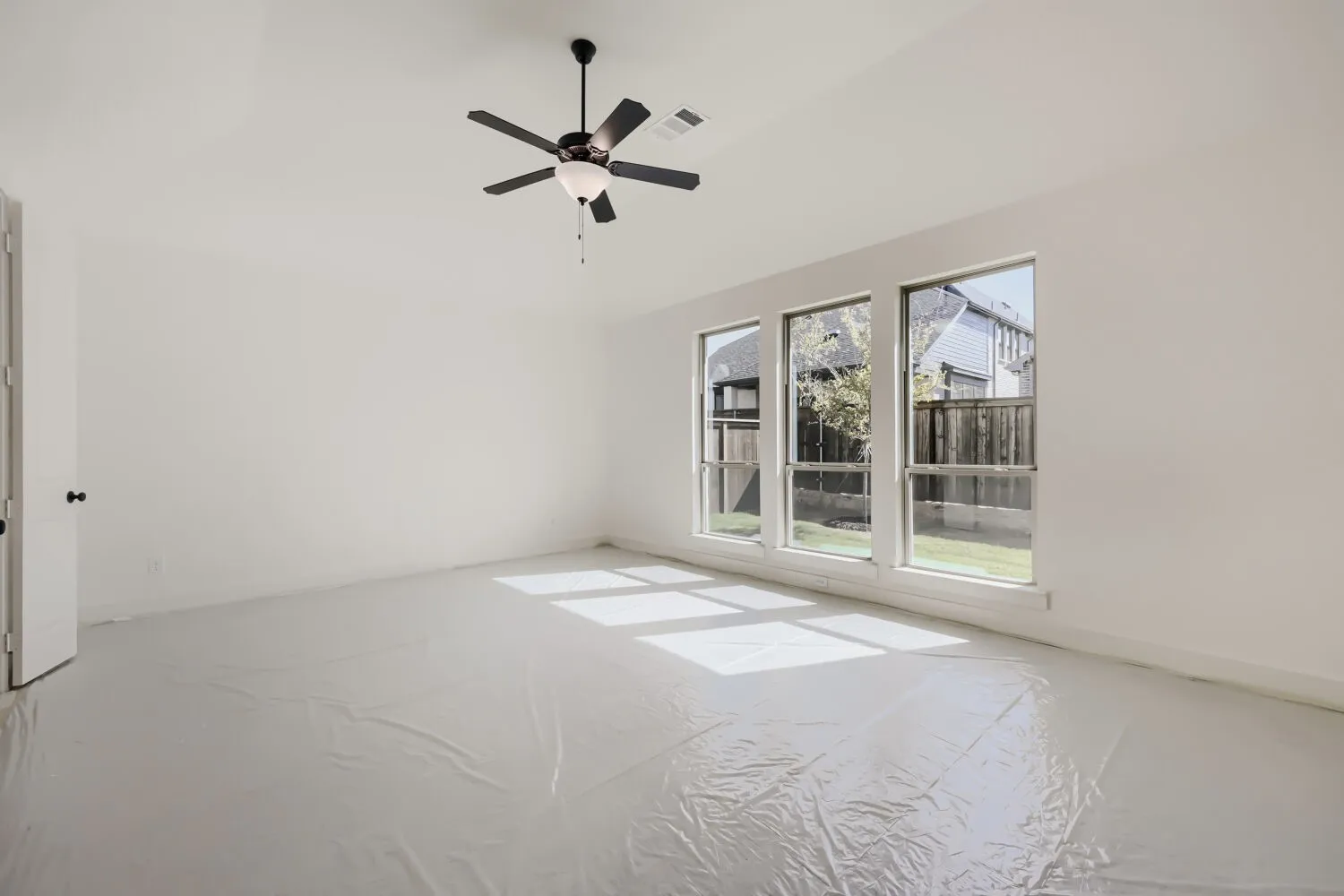 Bright interior space with a ceiling fan, three large windows, white walls, and a white door with black hardware
