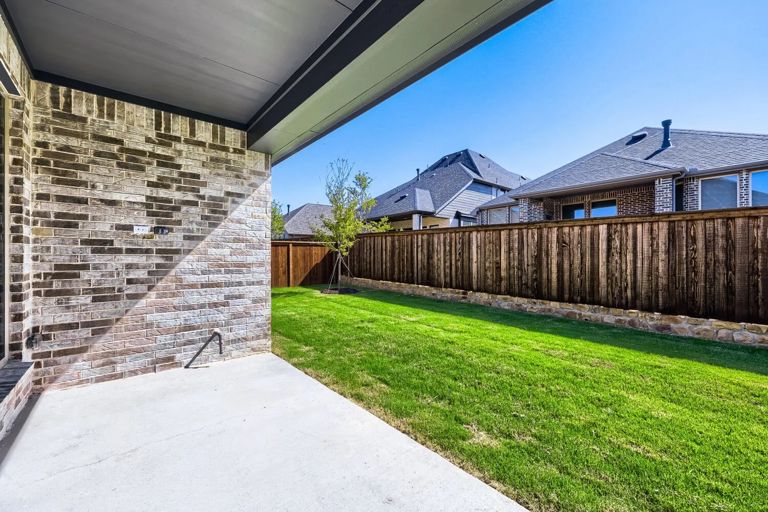 Covered patio with concrete flooring, brick exterior, and a private wood fence